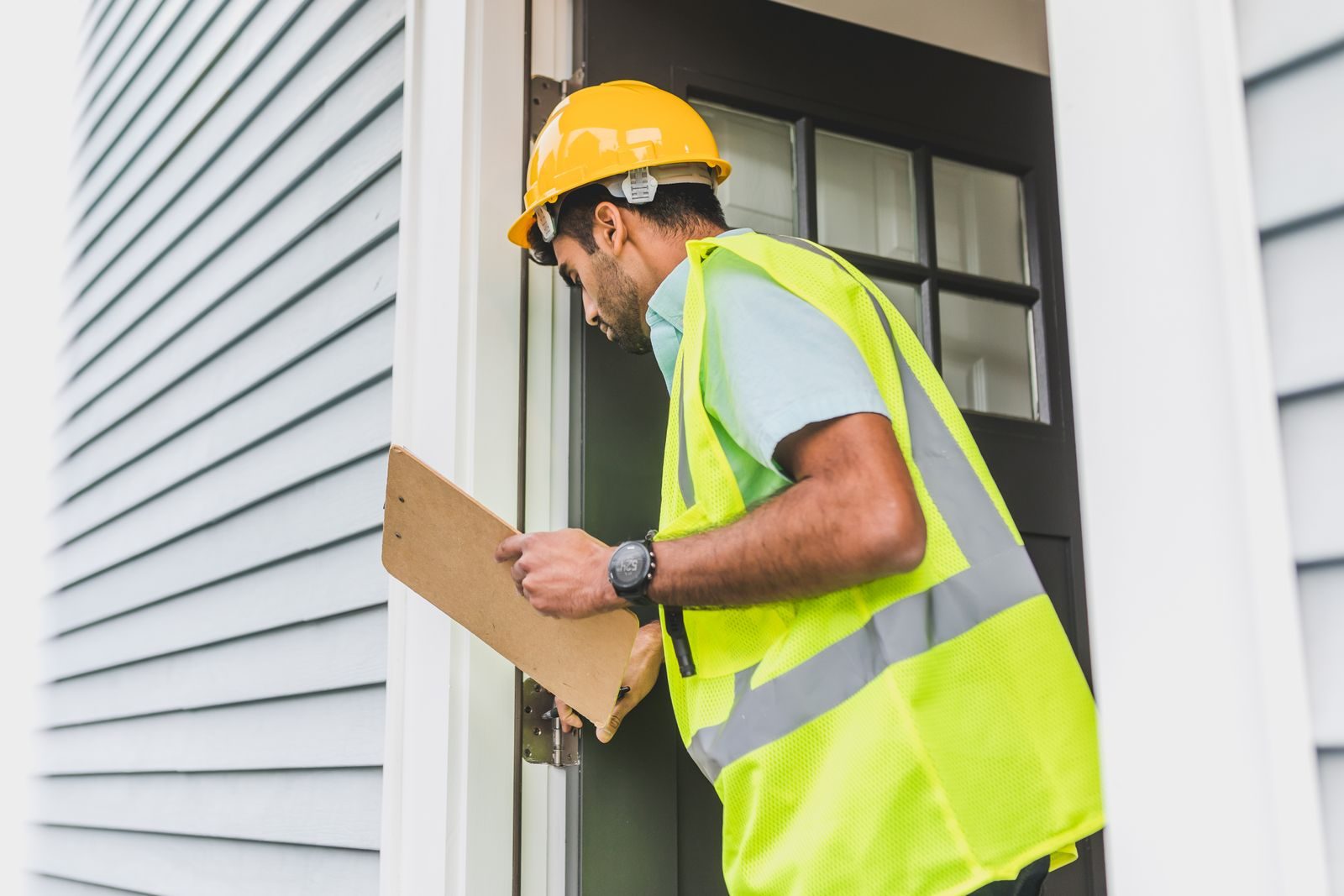 A male inspector in a hard hat conducts a property inspection outdoors with a clipboard