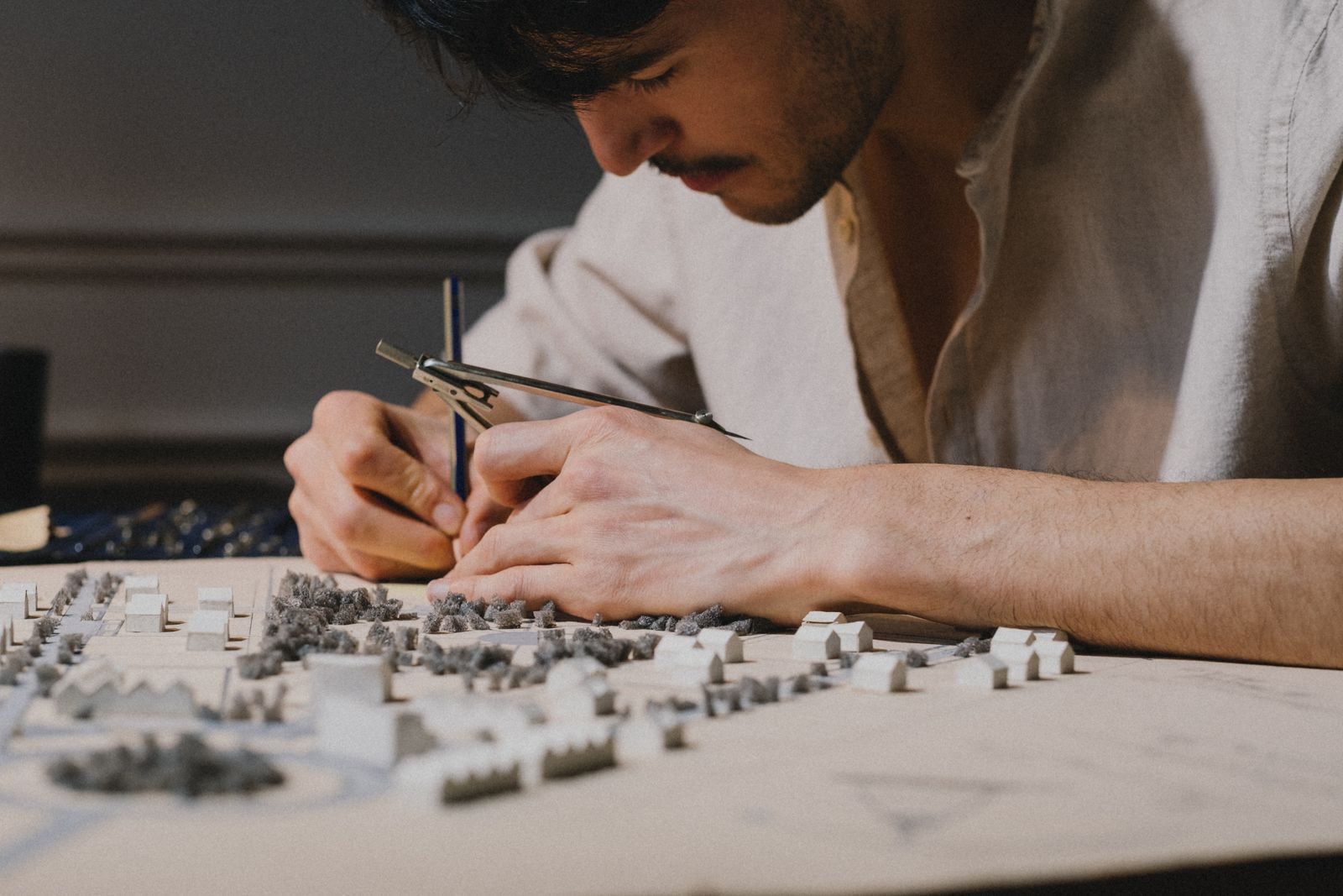Architect focused on creating a detailed model using a compass indoors, showcasing precision and creativity