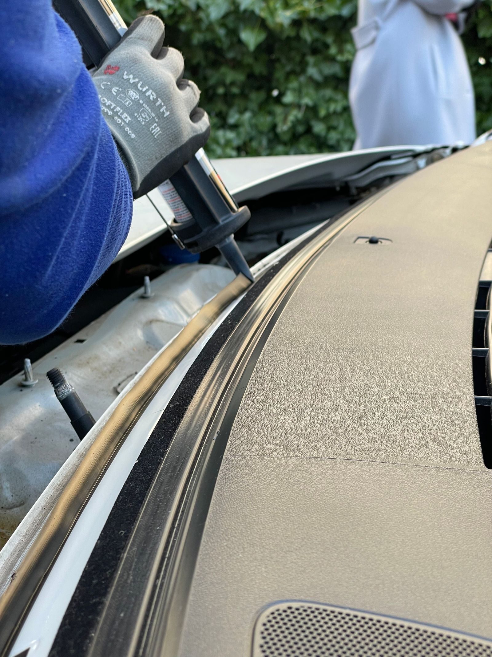 Close-up of a technician applying sealant to a car windshield in daylight