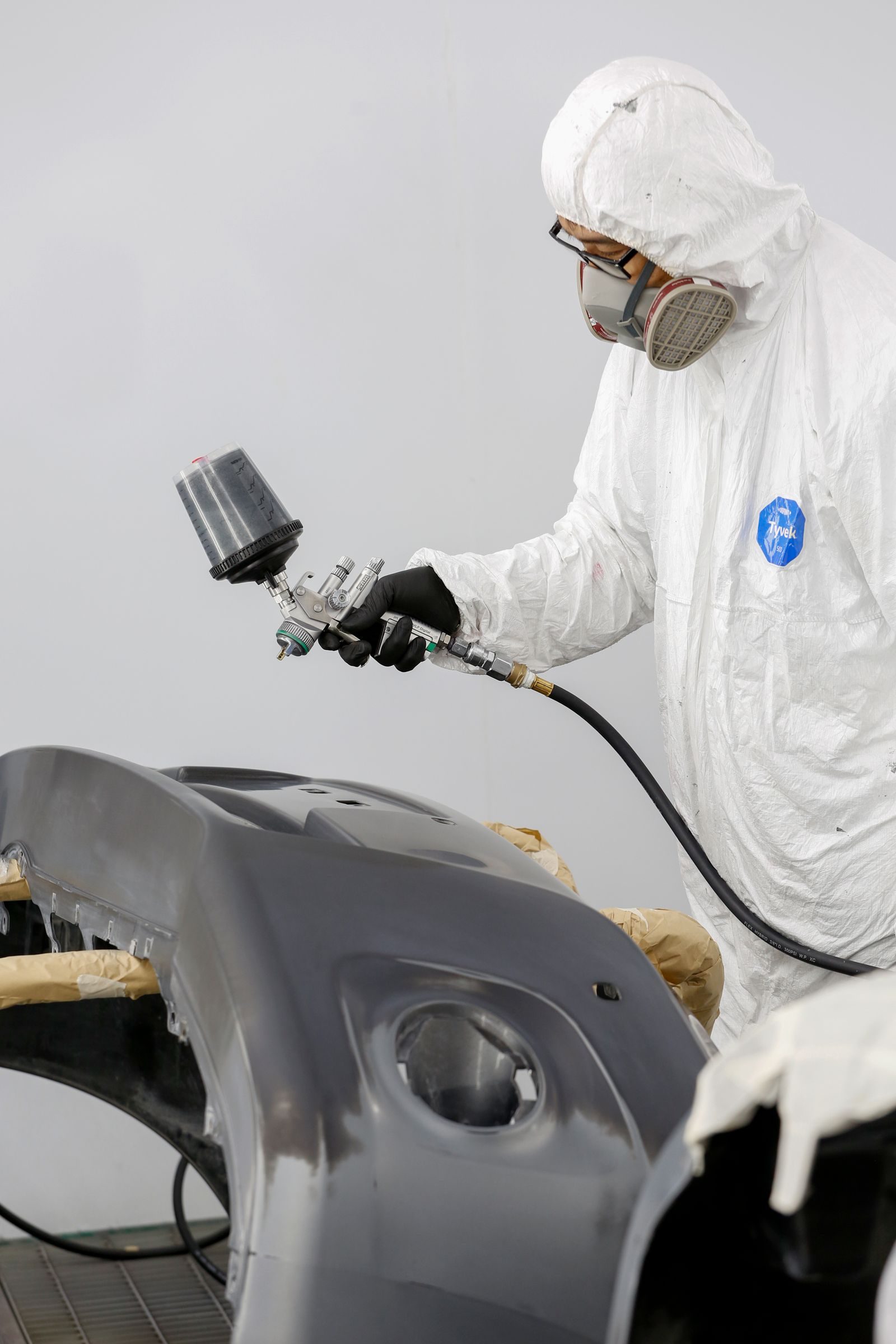 Technician in protective gear spray painting a car bumper