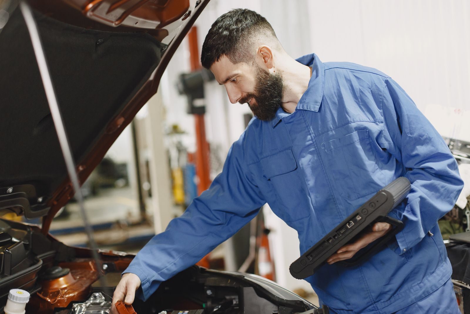 An auto mechanic in blue coveralls inspecting a car's engine in a garage