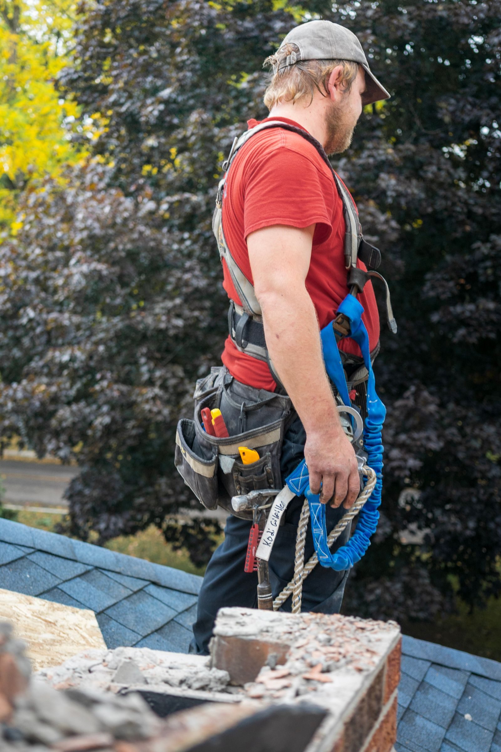 A construction worker with safety gear stands on a residential rooftop, inspecting a chimney