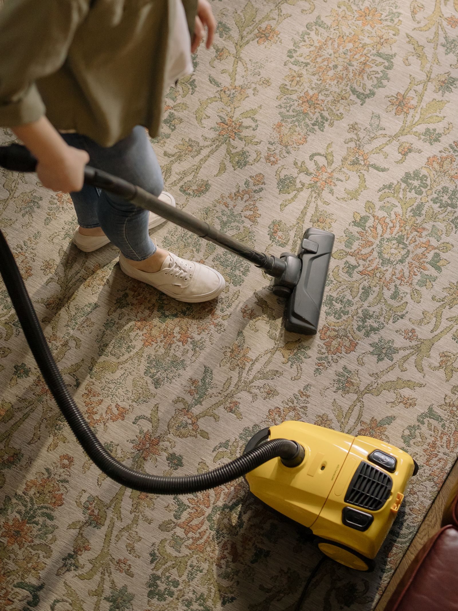 Person cleaning a floral carpet with a yellow vacuum cleaner indoors