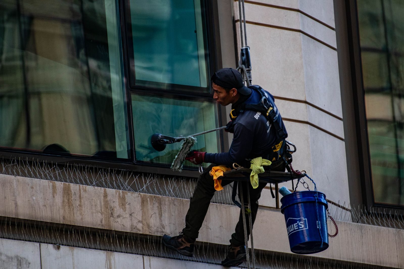 Man cleaning high-rise building windows using safety harness outdoors in daylight