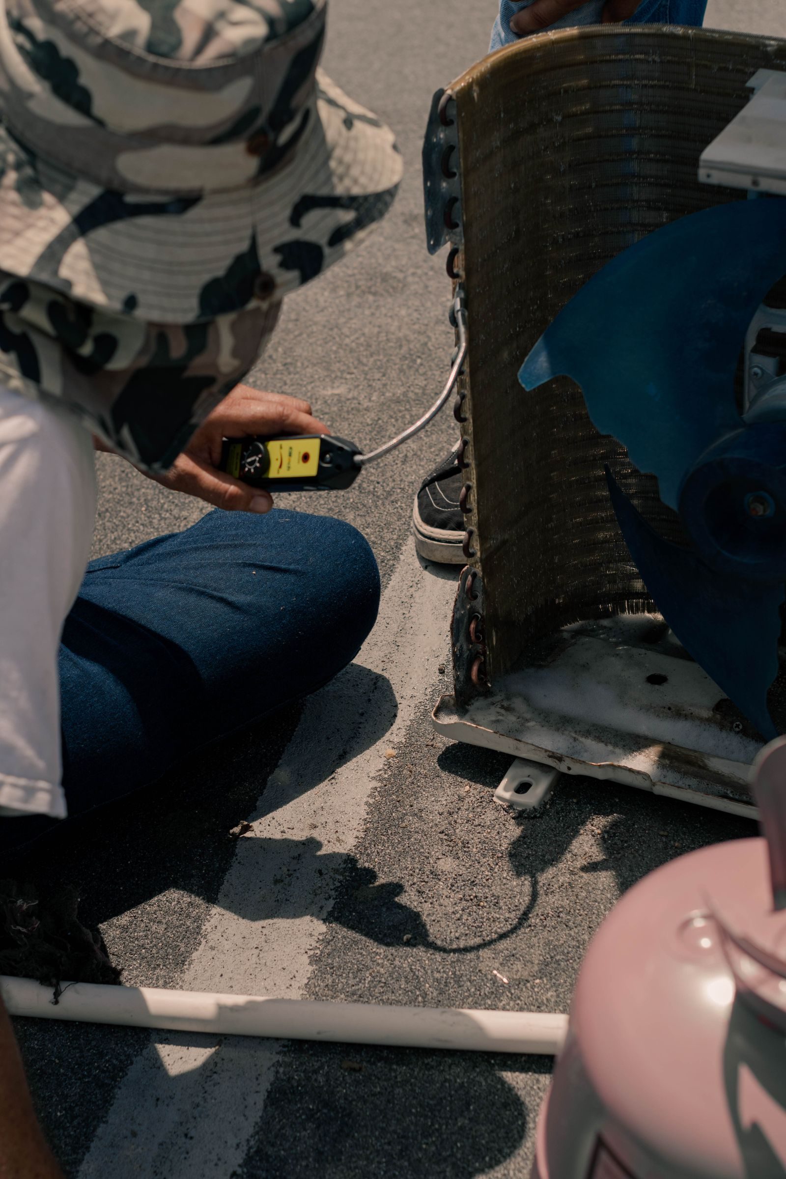 A technician kneeling at a rooftop air conditioning unit with a meter