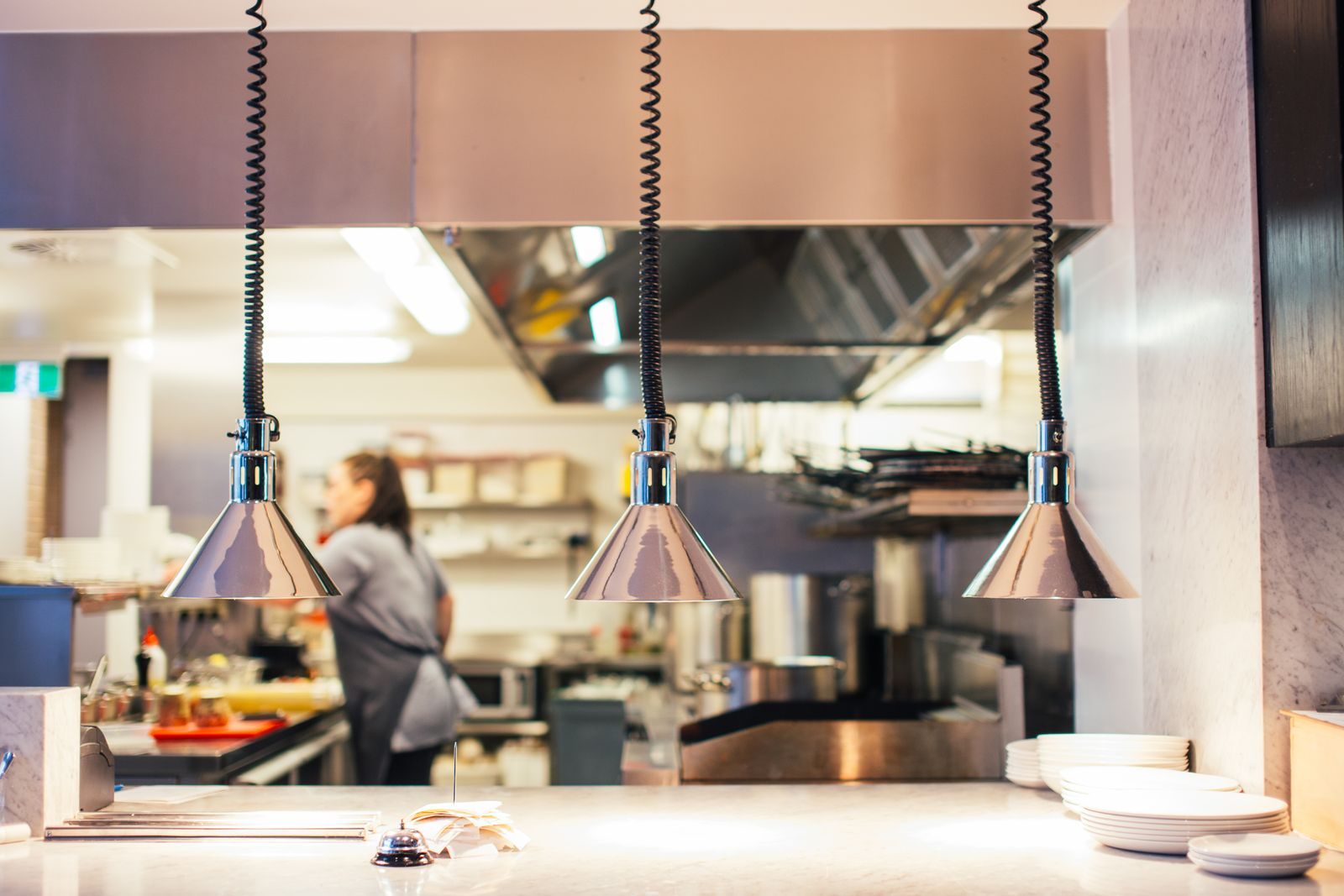 Side view of unrecognizable female chef in restaurant kitchen working behind counter with infrared lamps and s