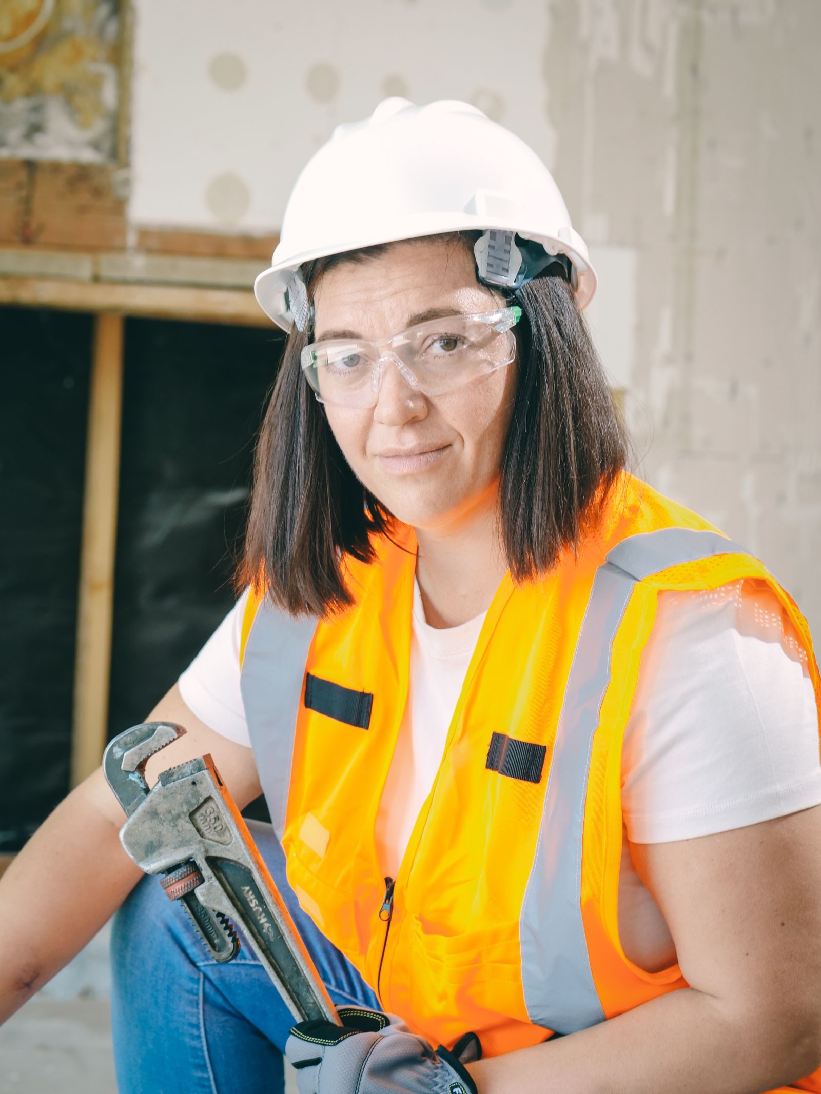 Female construction worker wearing PPE, holding a wrench in an indoor setting