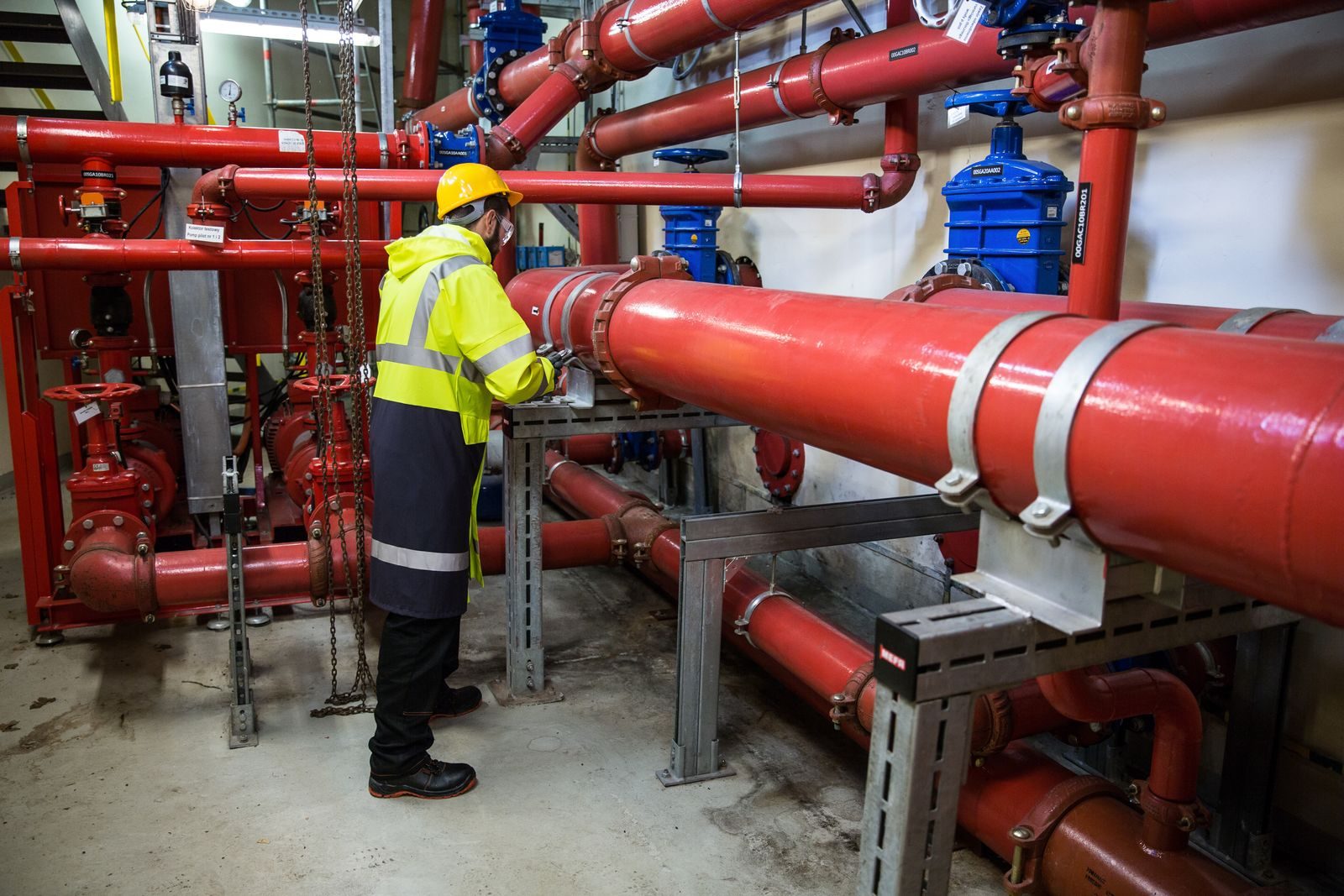 Engineer with safety gear inspecting red industrial piping system indoors