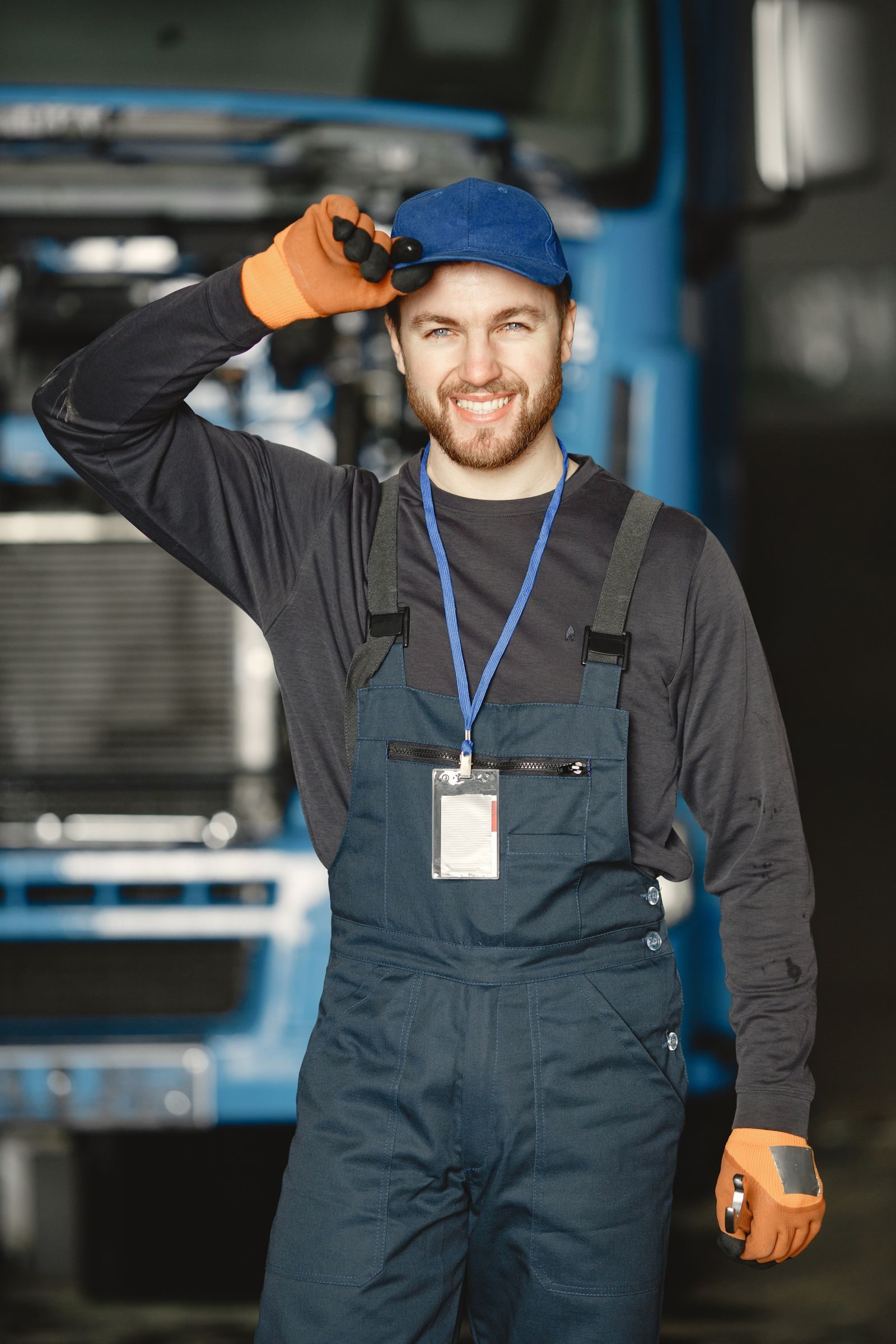 Friendly mechanic in uniform saluting in front of a truck at workplace
