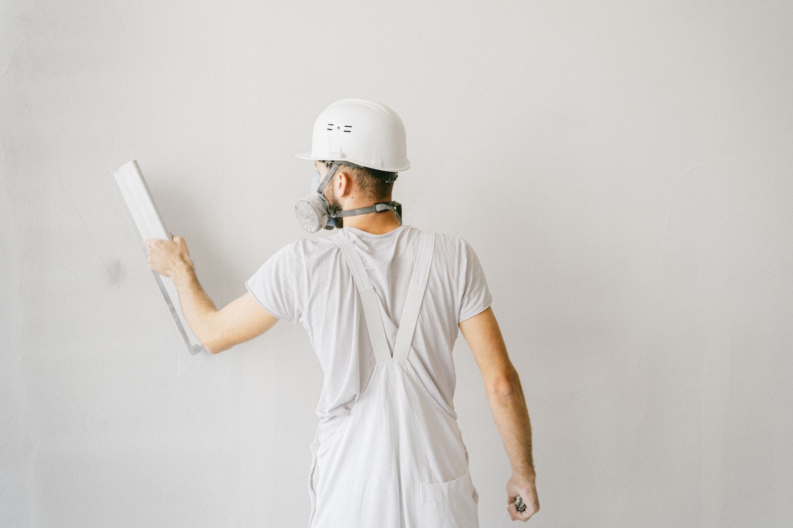 Back view of a construction worker in safety gear plastering a white wall