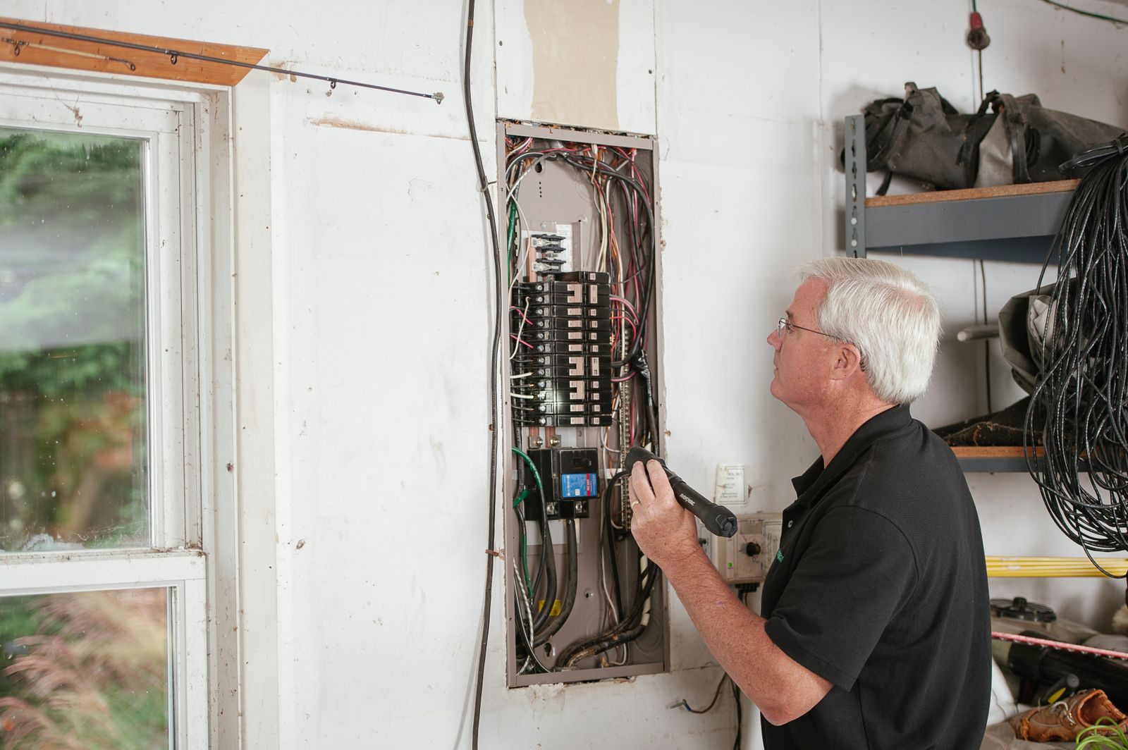 An electrician carefully examines a residential fuse box indoors, ensuring electrical safety and compliance
