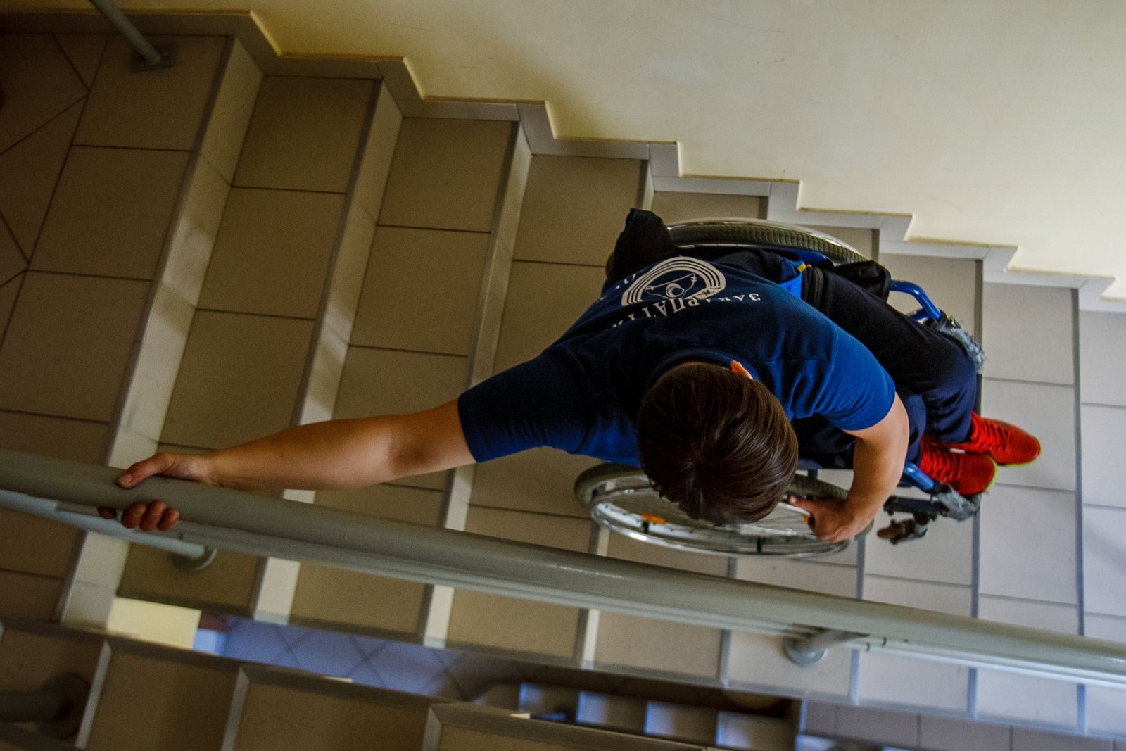 Overhead view of a person in a wheelchair going down stairs indoors, holding onto railings