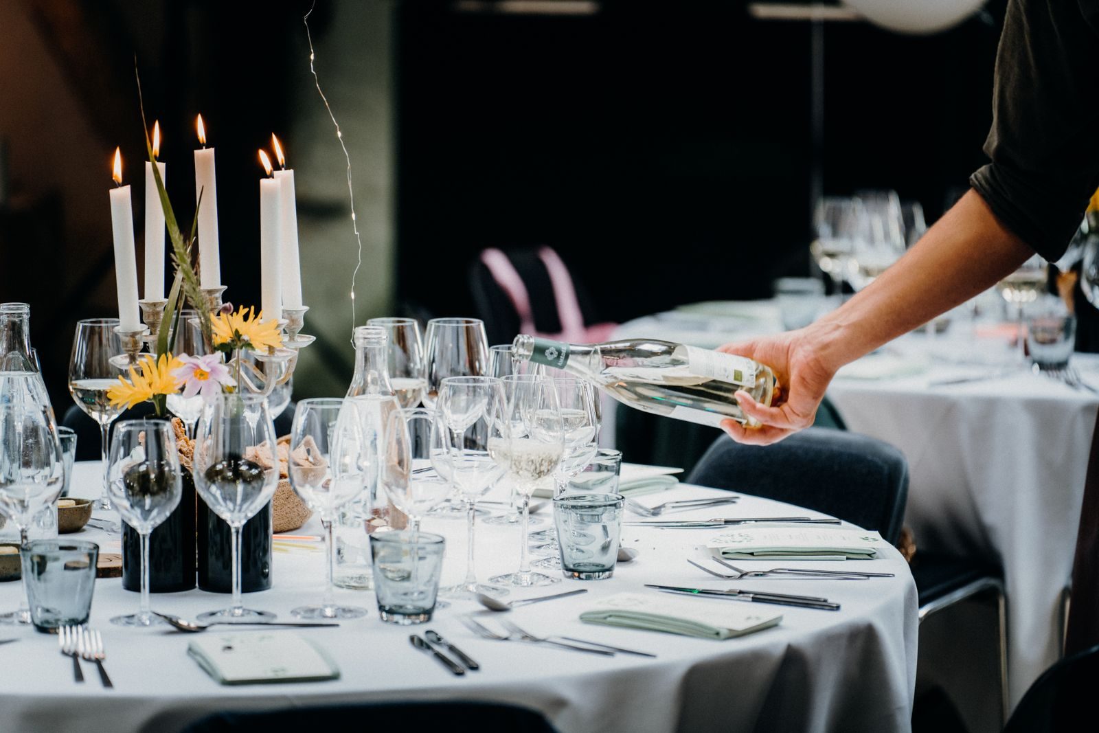 A beautifully set dinner table with a hand pouring white wine, perfect for celebrations