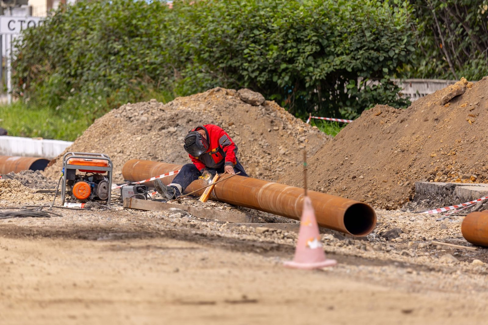 A construction worker welds a large pipe on a sunny day at an outdoor site