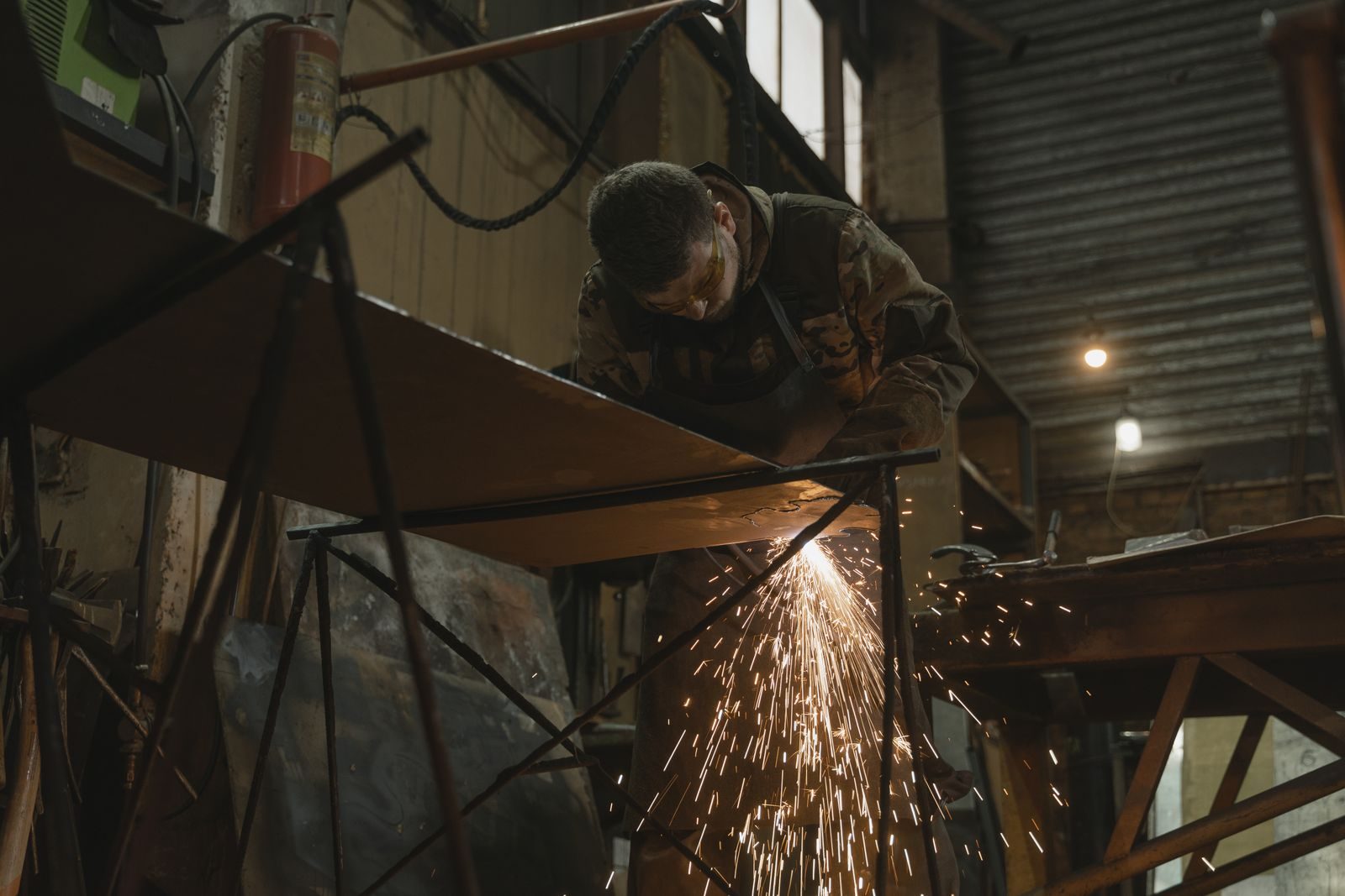 A worker focused on welding metal inside an industrial setting with sparks flying