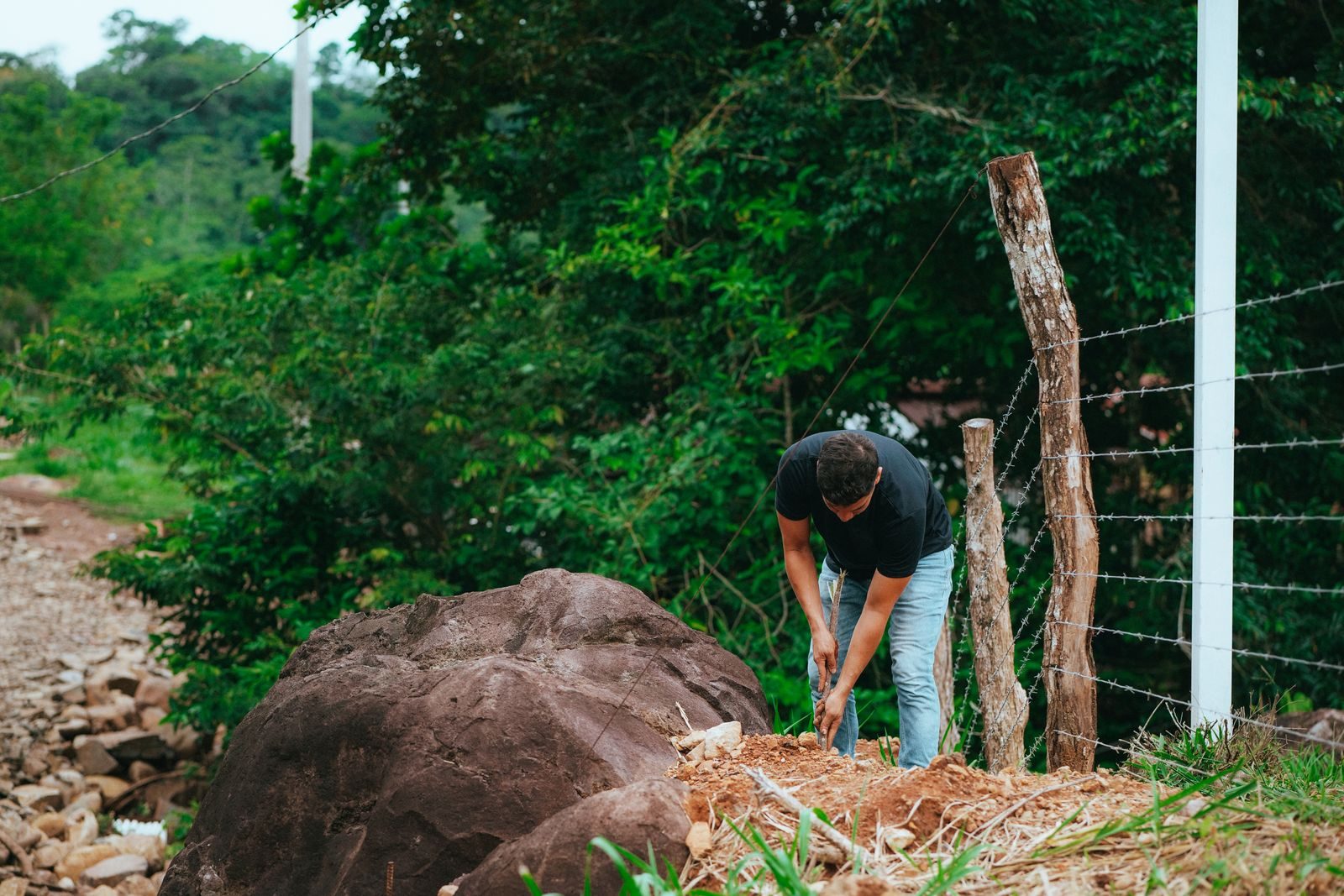 A man working near a barbed wire fence in a natural landscape, embodying outdoor labor