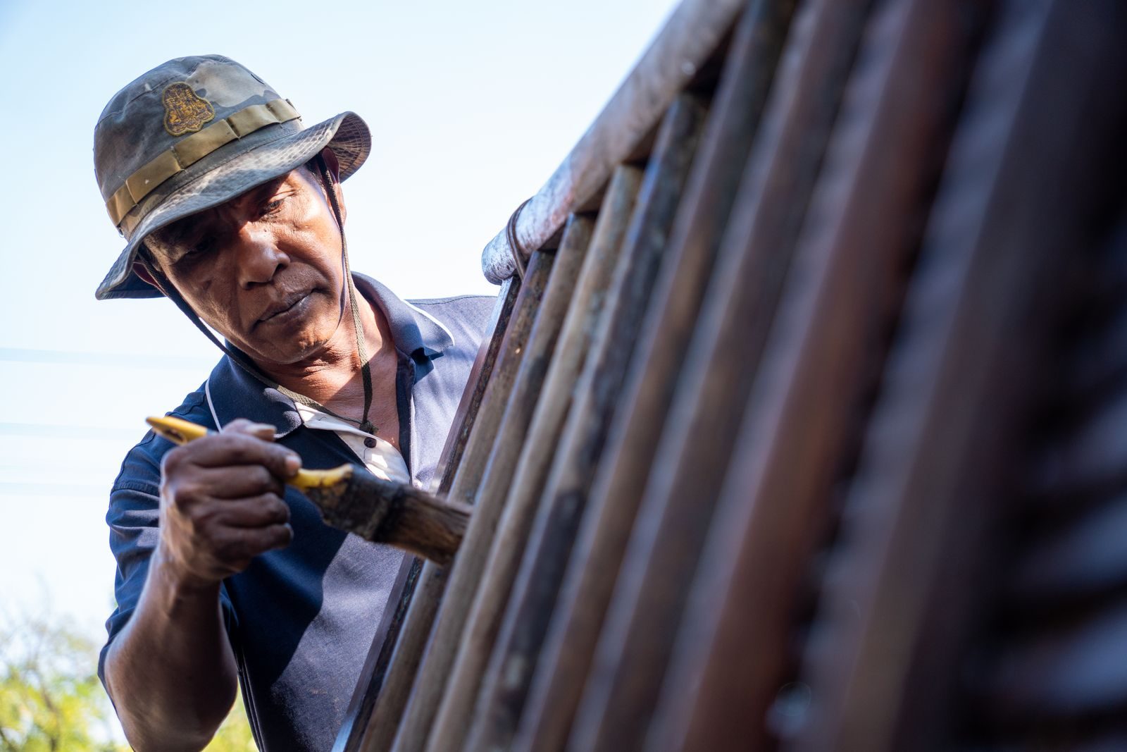 Outdoor scene of a man painting a wooden fence with a brush, emphasizing craftsmanship