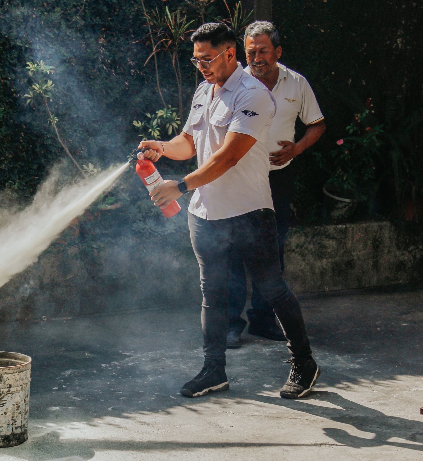 Two men demonstrating fire extinguisher use outdoors in daylight