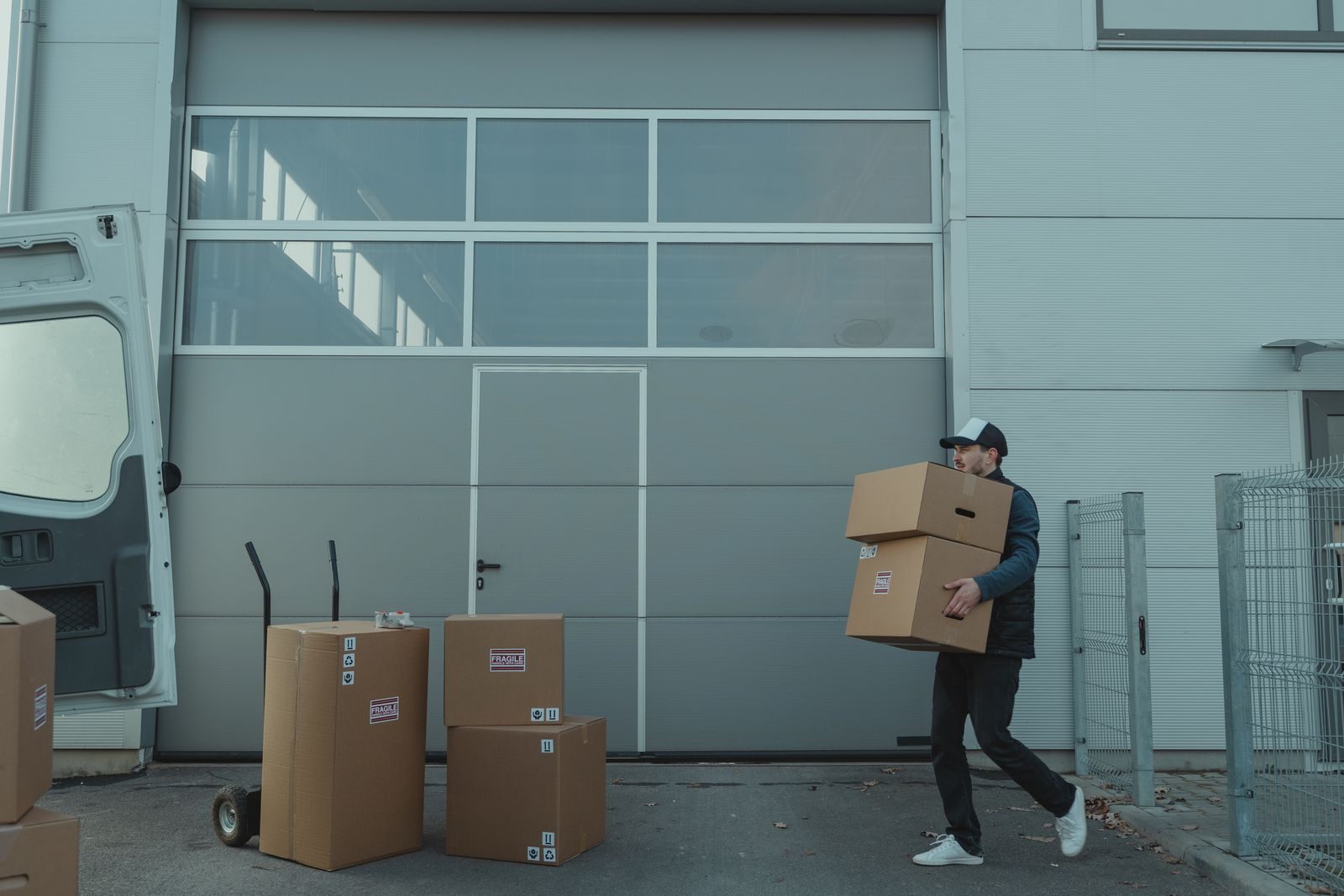 A delivery person carrying cardboard boxes outside a warehouse facility