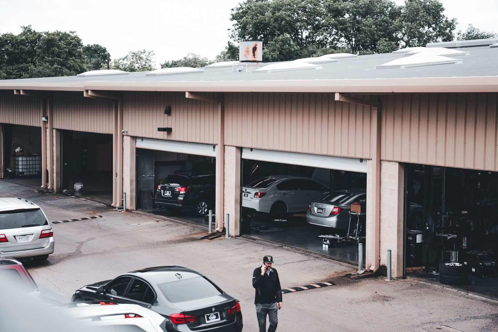 A man walks by a garage with cars parked inside and outside in an urban setting