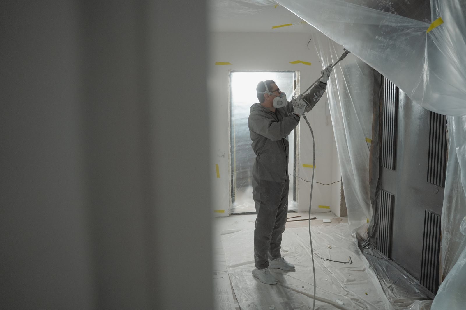 Man in protective gear spray painting a house's interior during renovation work