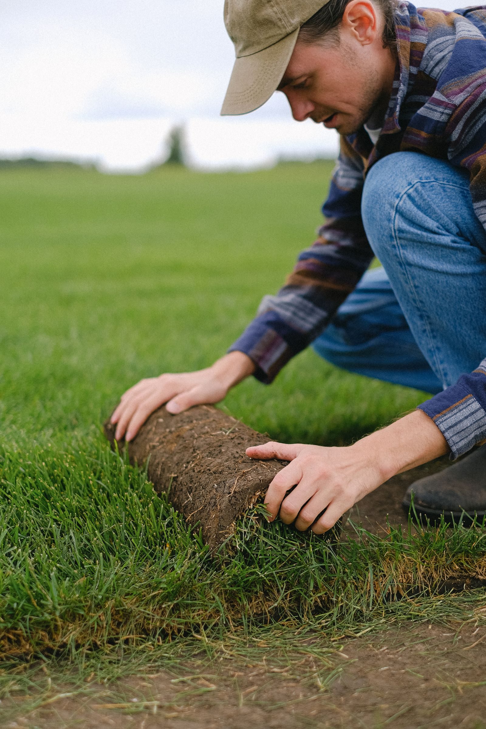 Side view of male worker laying sod grass onto ground for new garden lawn while working in countryside on blur