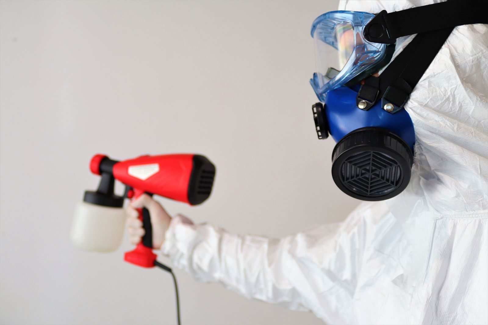 A worker in protective gear uses a disinfectant spray indoors