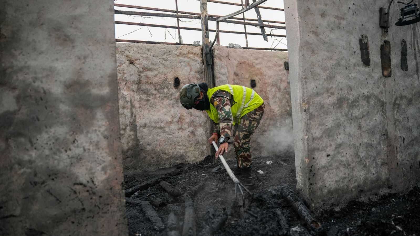 A firefighter in protective gear cleans debris in the aftermath of a fire inside a building