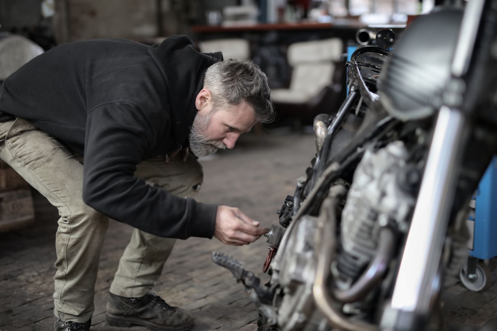 Side view of serious male master in untidy casual clothes standing near motorbike and checking details while w