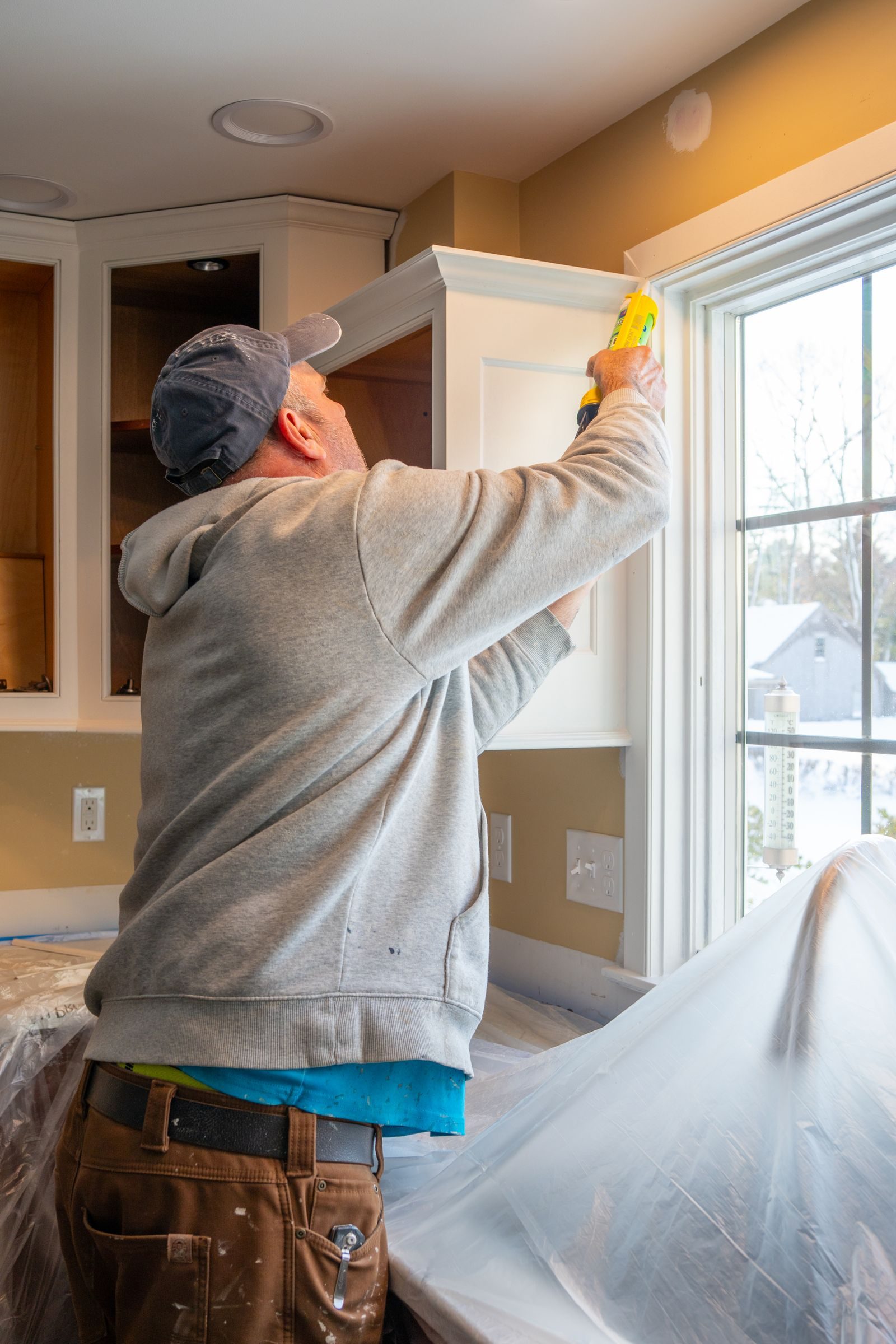 Man caulking kitchen cabinet during home renovation in Quincy, Massachusetts, USA