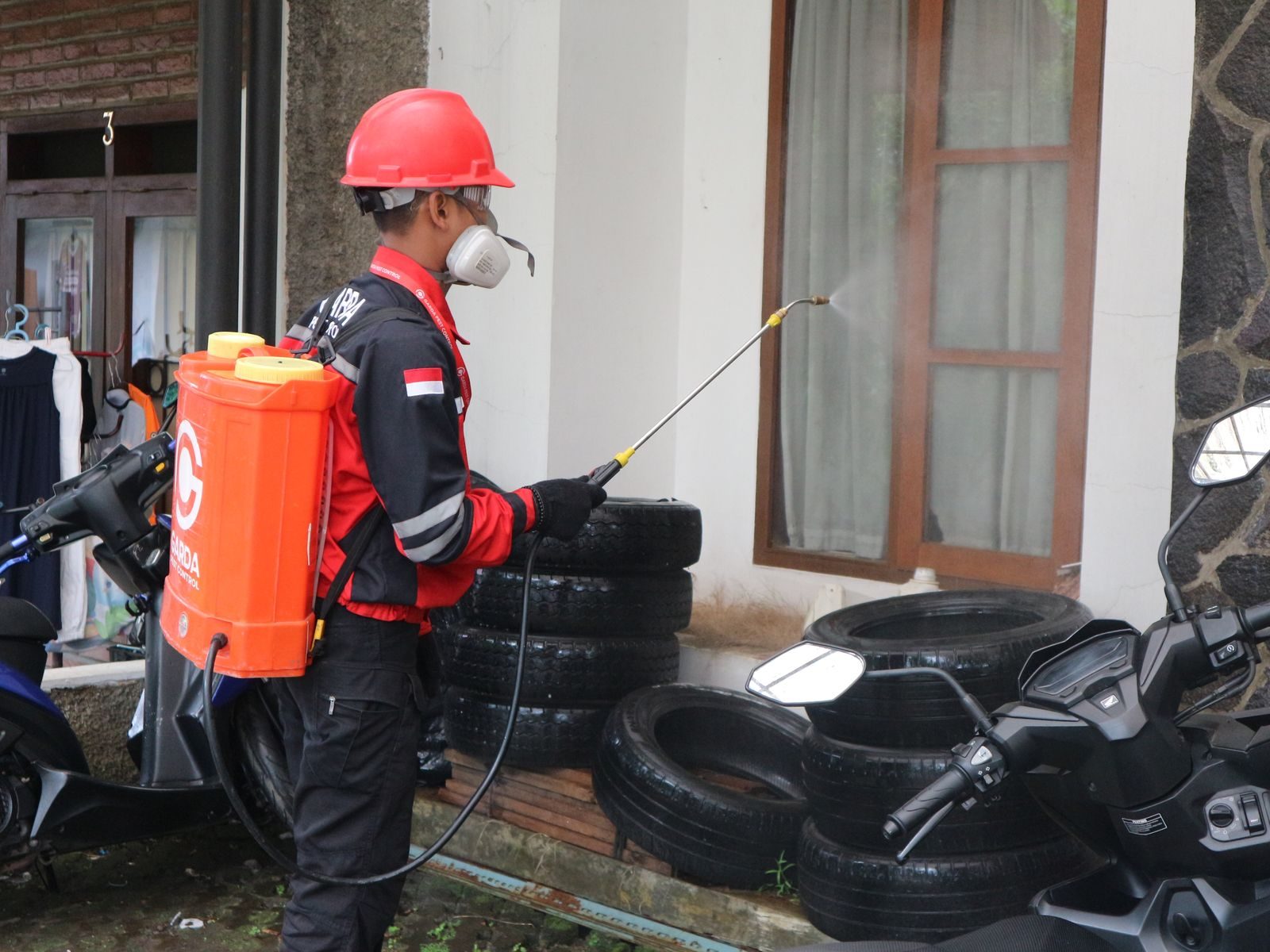 A worker in safety gear sprays disinfectant outside a building, ensuring cleanliness