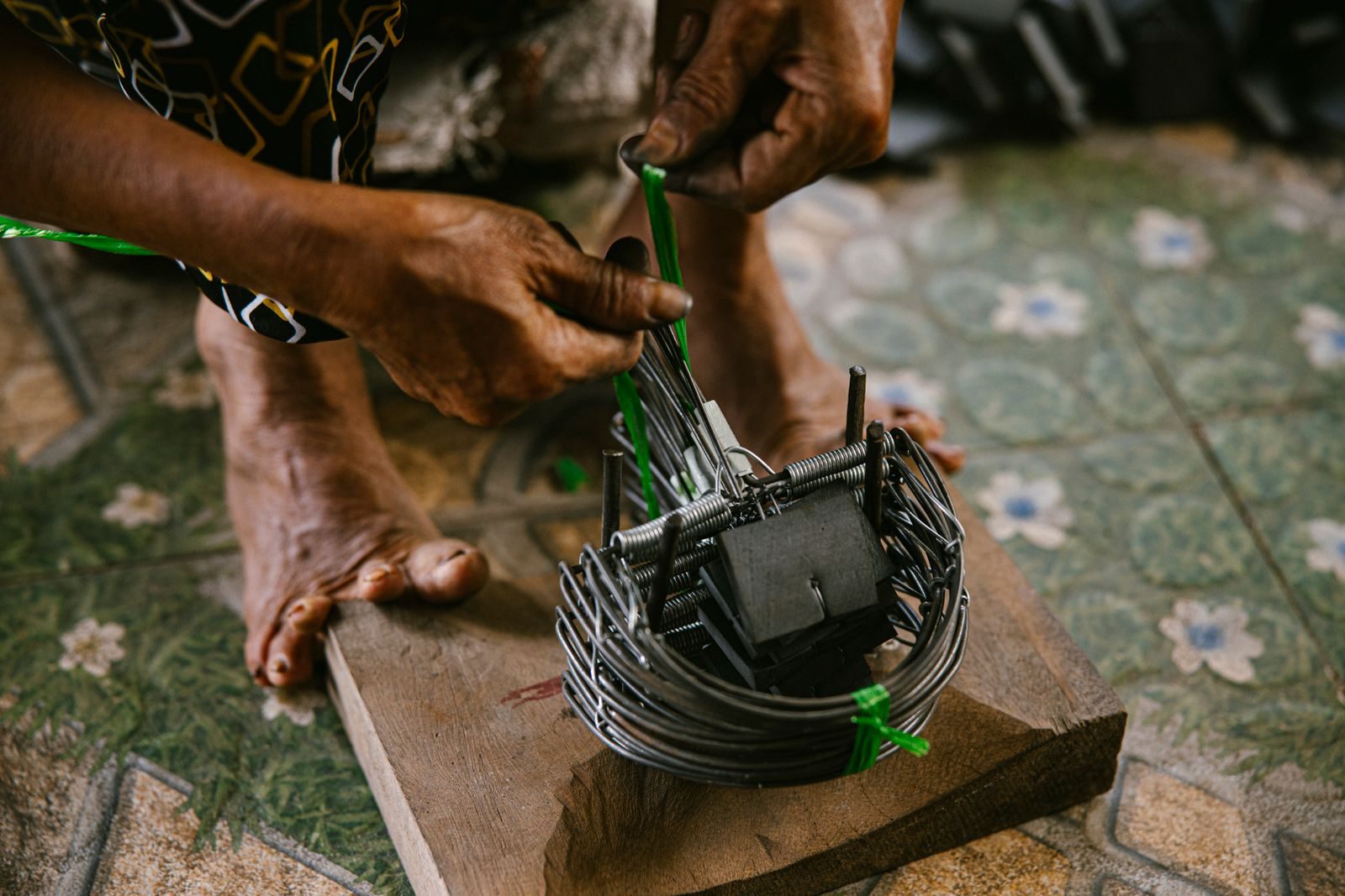 Craftsman's hands skillfully weaving a metal trap on wooden base indoors. Traditional craftsmanship