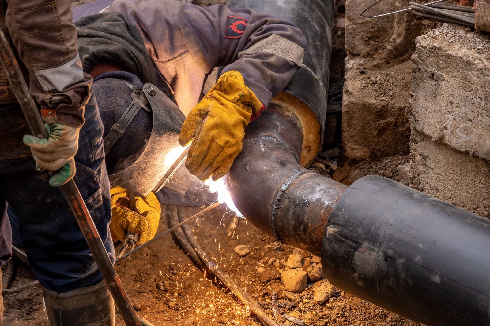 Close-up of a skilled worker welding steel pipes in an industrial setting, showcasing expertise and safety gea