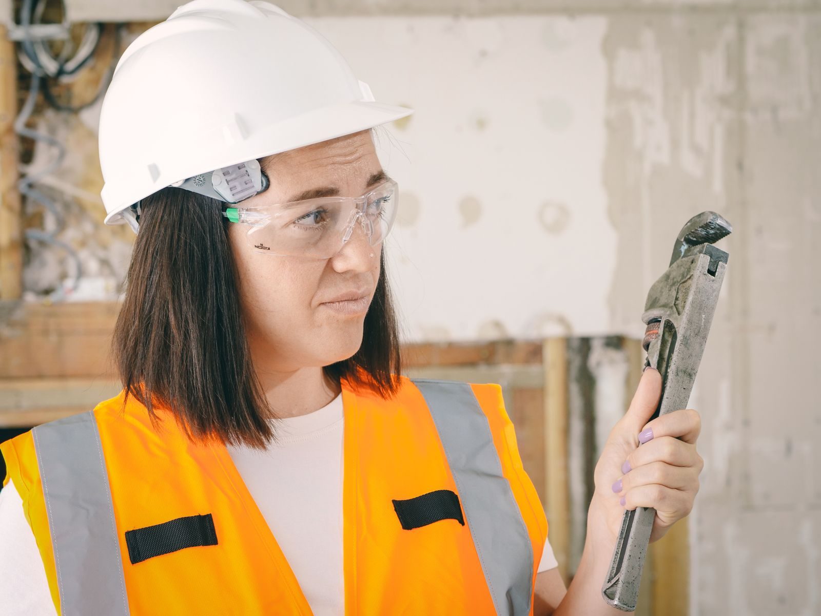 Caucasian woman in PPE holding a plumber's wrench indoors, focused on maintenance