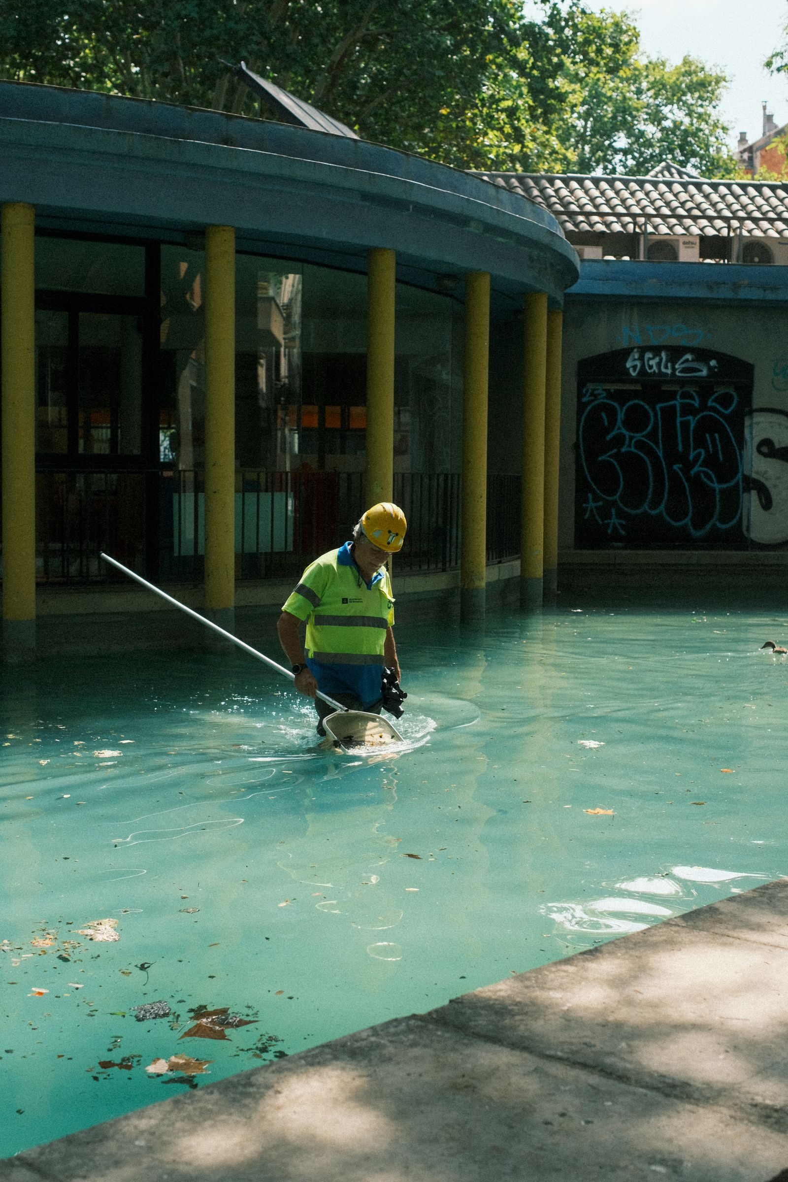 A pool maintenance worker in safety gear cleans an outdoor pool