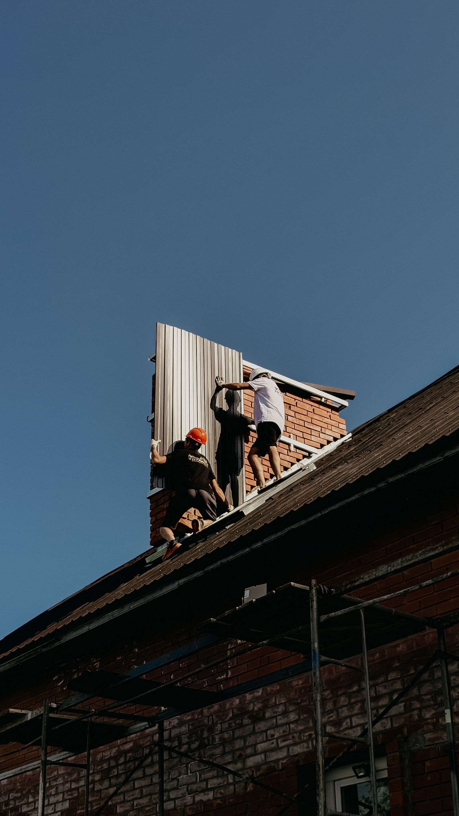 Workers installing roof panels on brick house