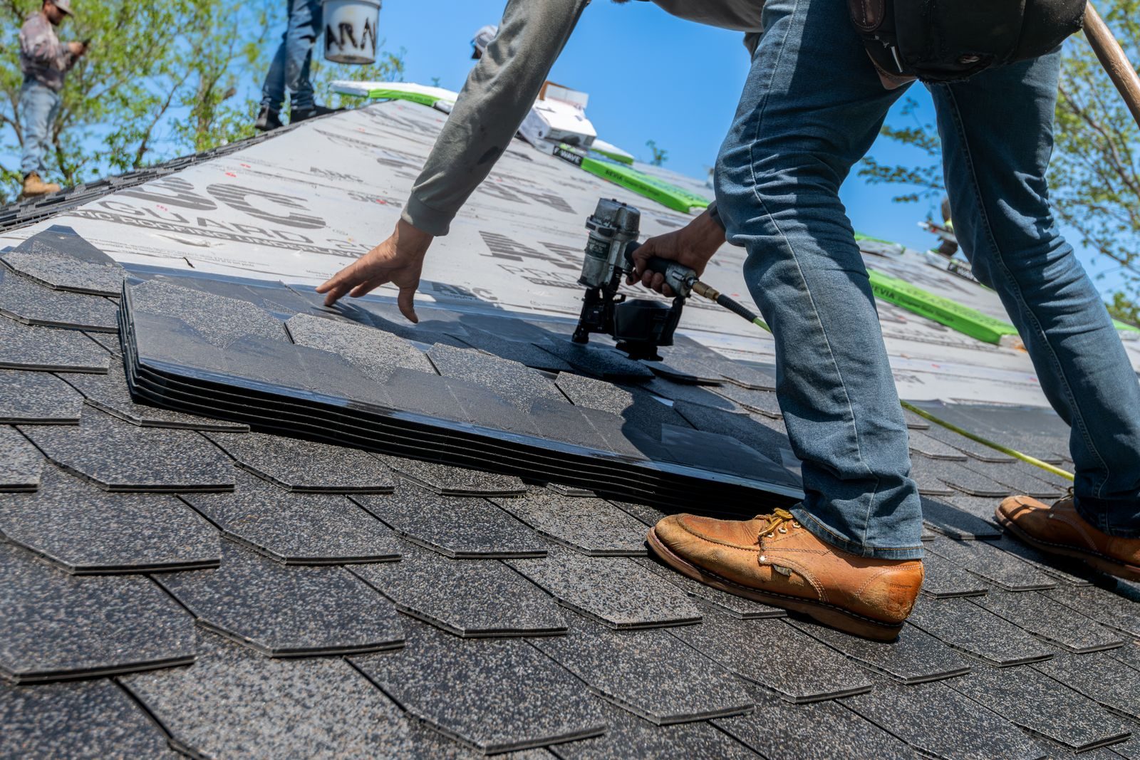 Roofer using nail gun for shingle installation on residential roof