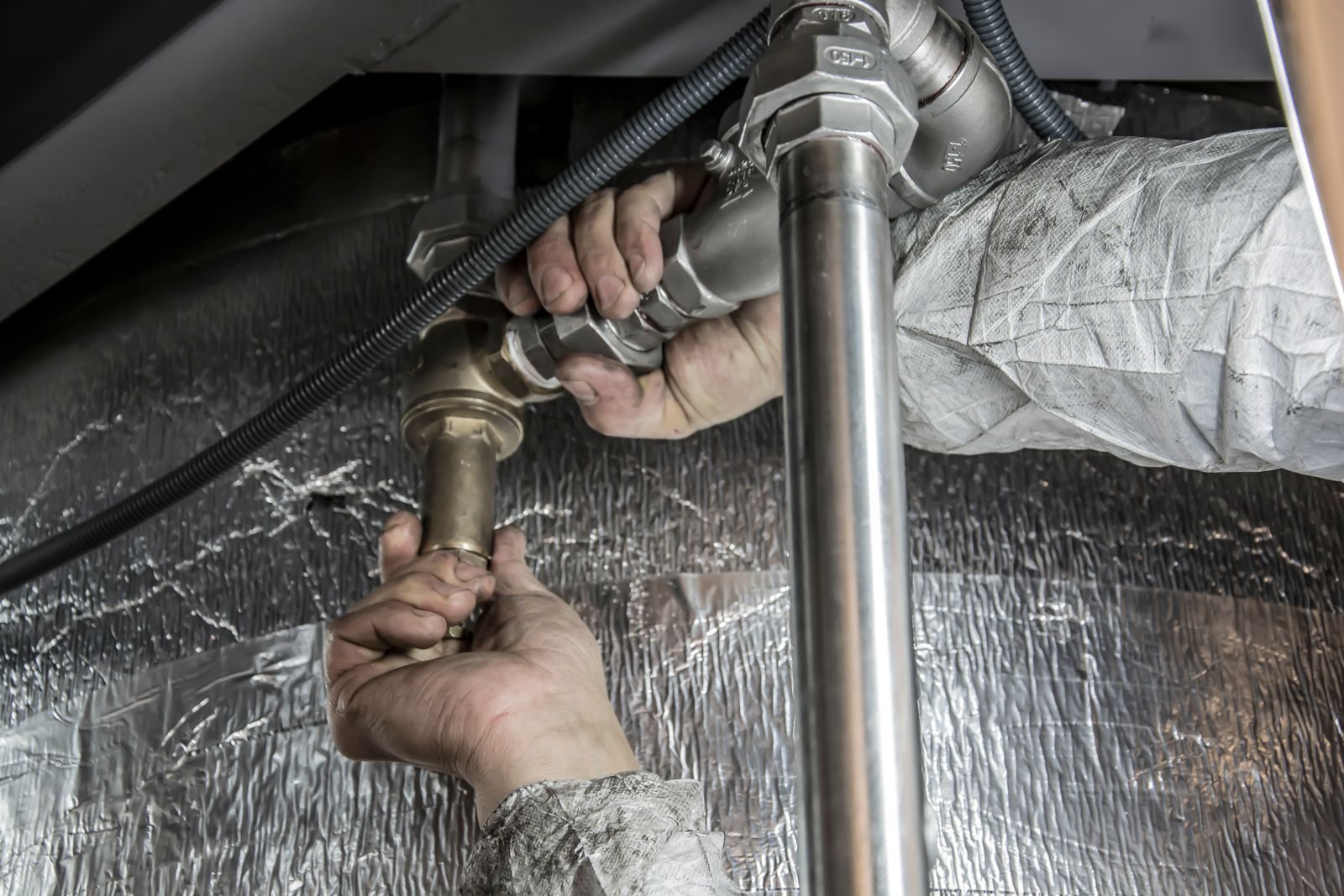 Close-up of a plumber's hands installing steel pipes indoors, showcasing skilled manual work