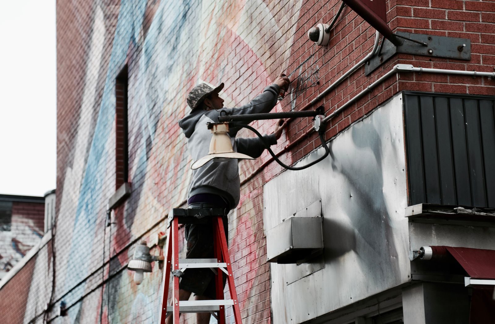 A worker on a ladder installs a security camera on a brick wall