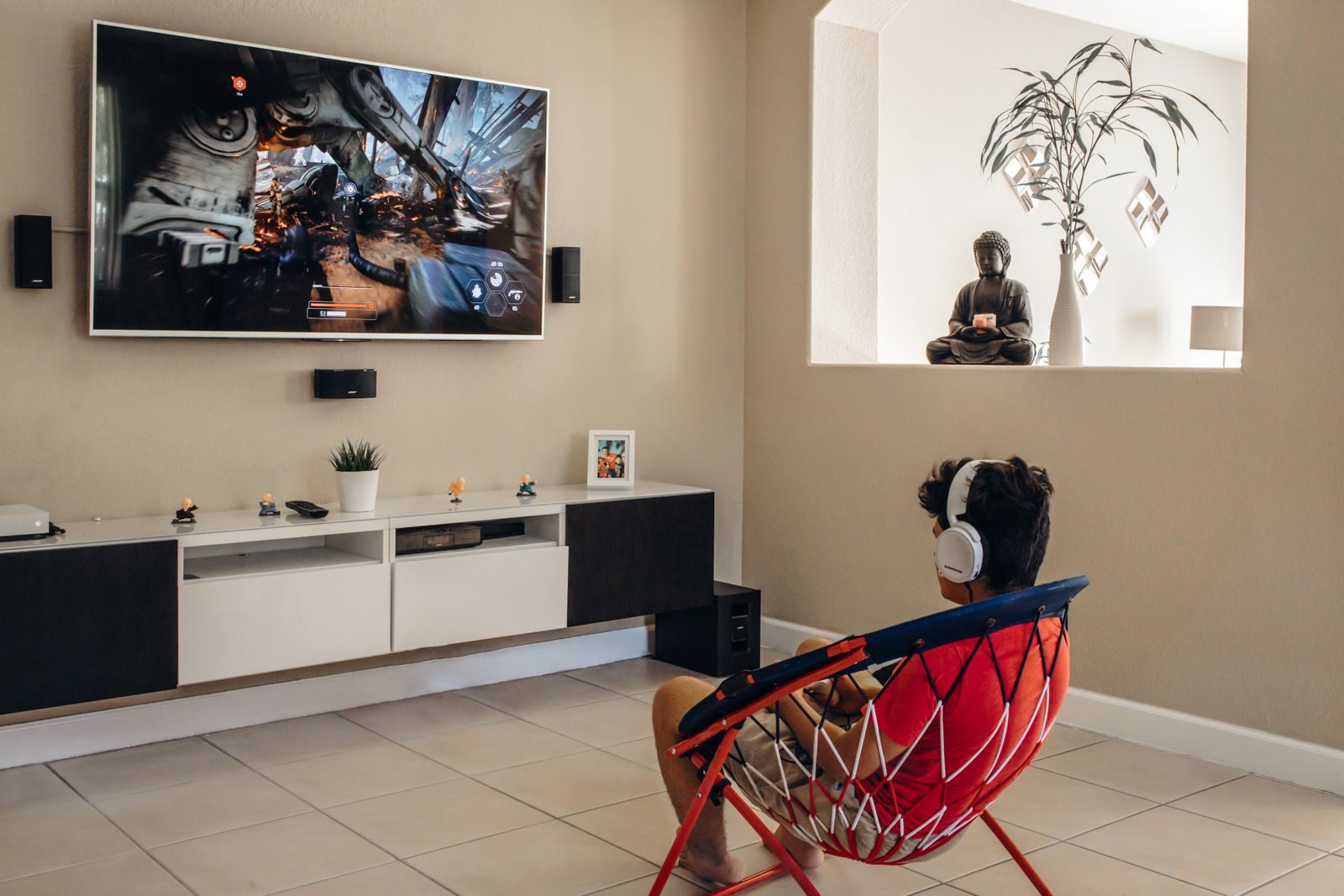 A young man wearing headphones plays video games in a modern living room setup