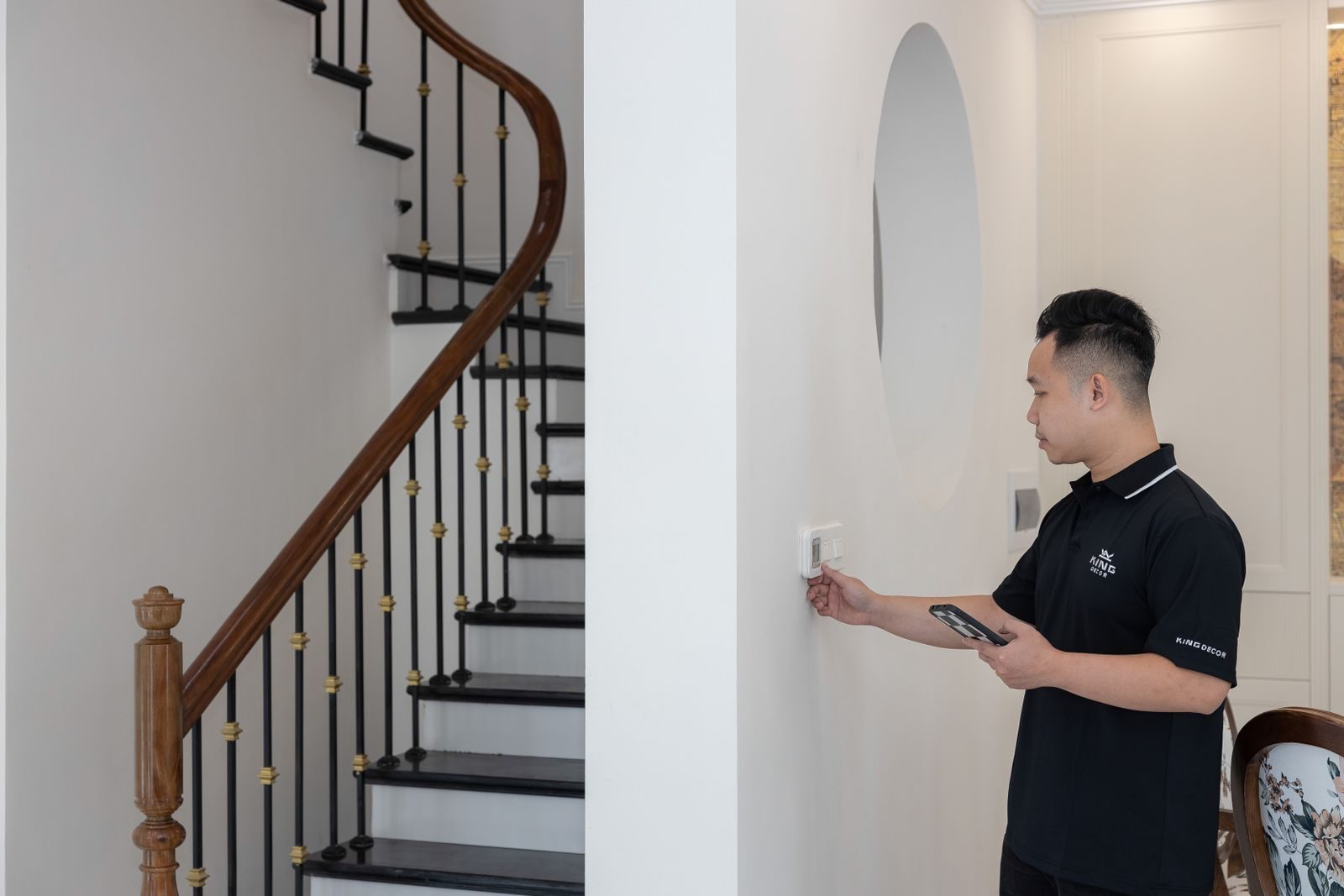 Man adjusting thermostat in stylish home with elegant staircase