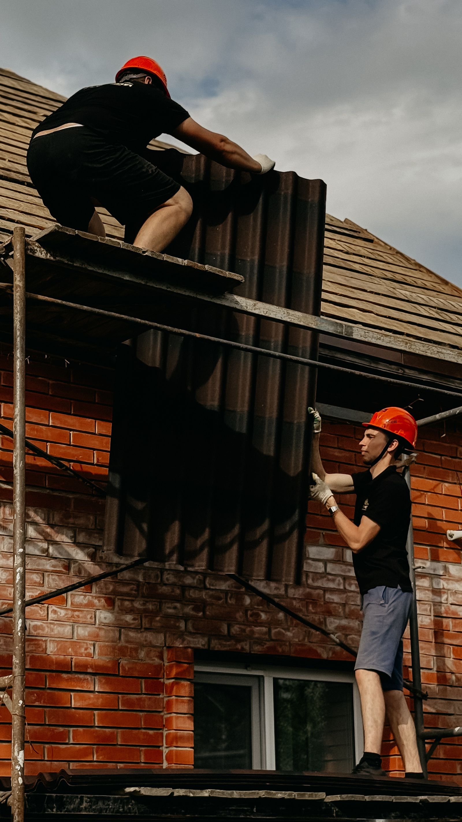 Construction workers installing roof panels on scaffold