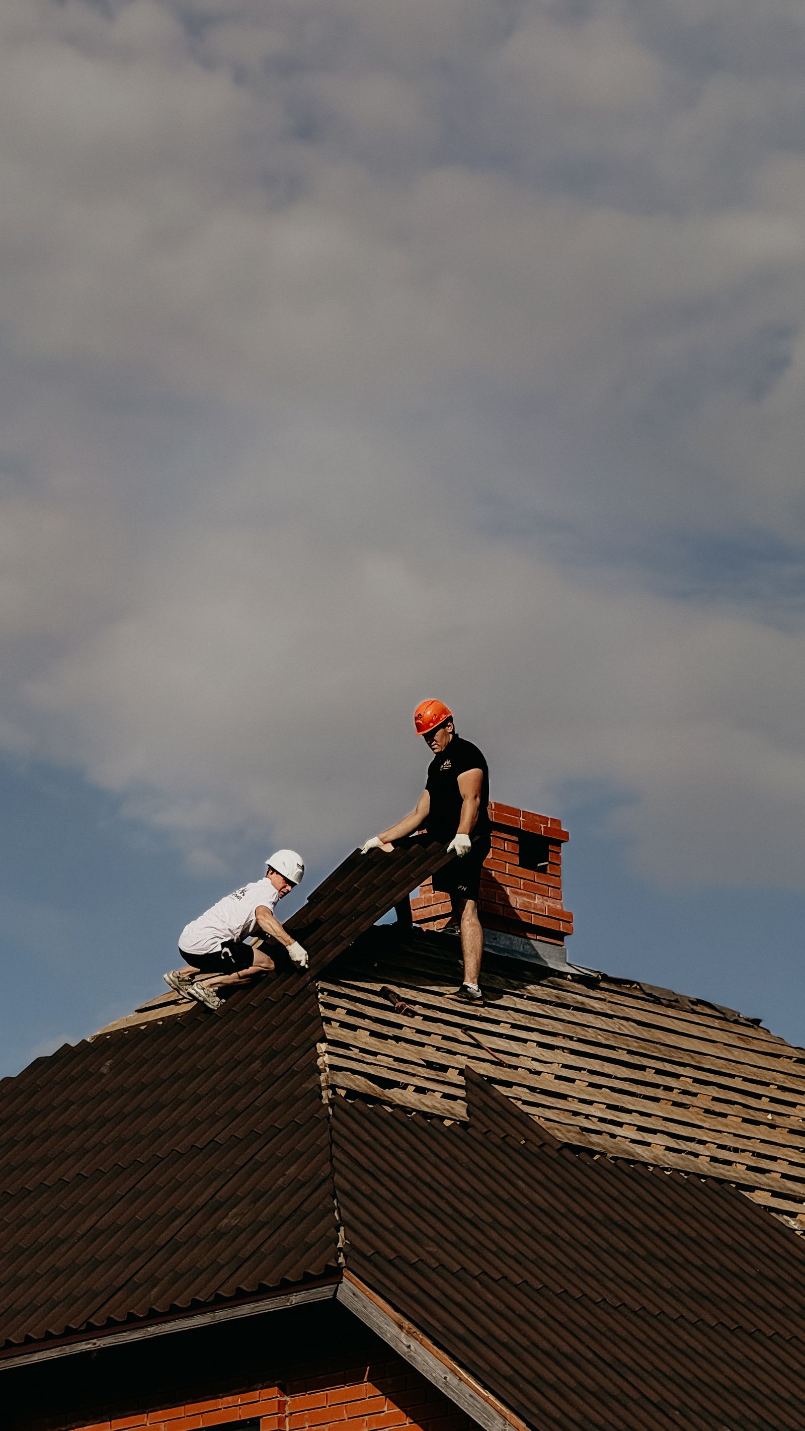Construction workers repairing roof under cloudy sky