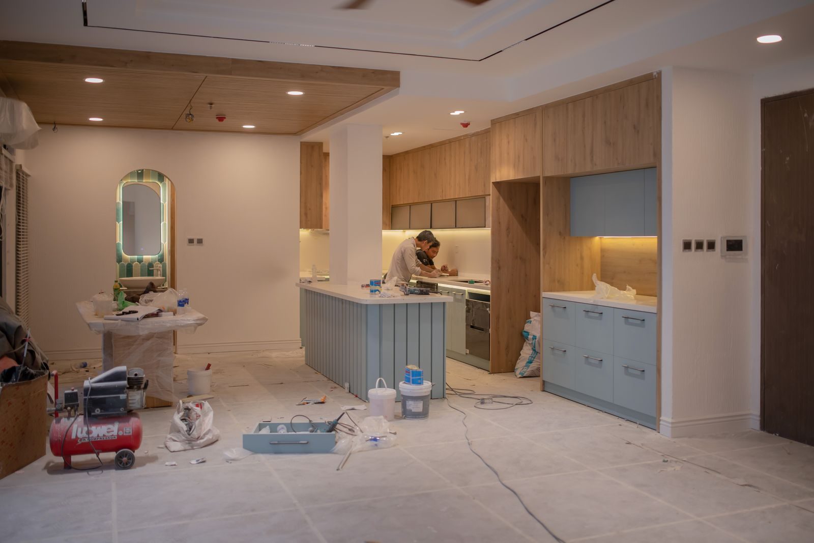 A modern kitchen undergoing renovation, featuring a worker, tools, and materials