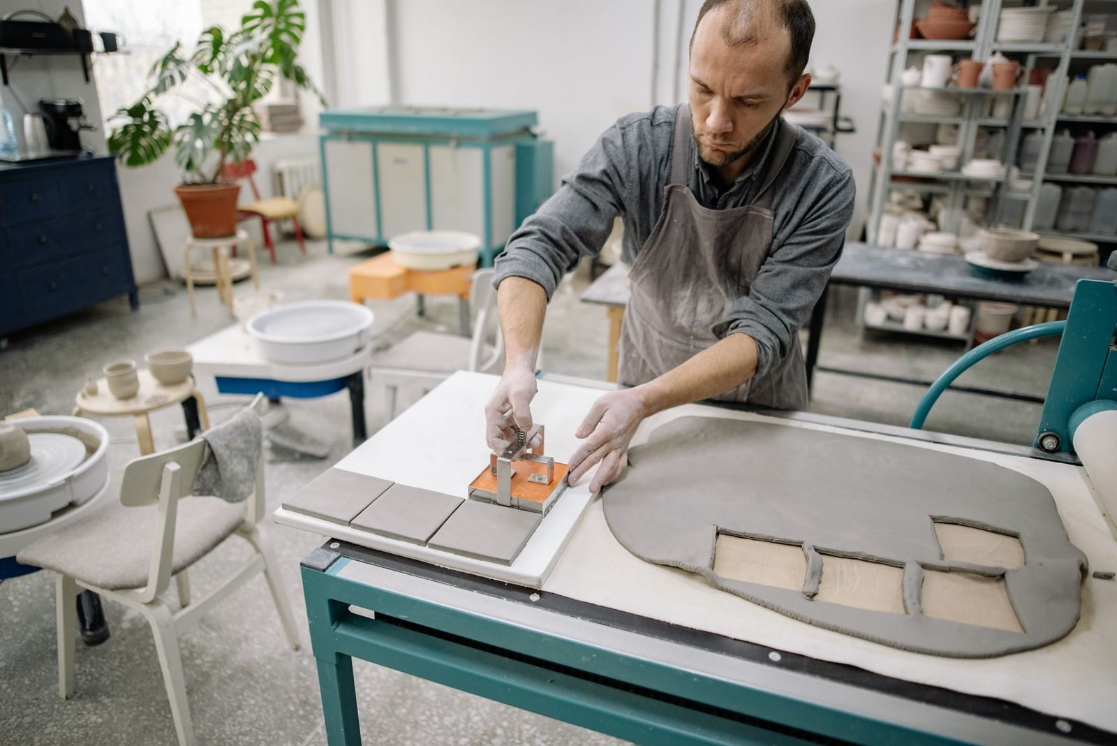 An adult man crafting pottery in a workshop using a clay press