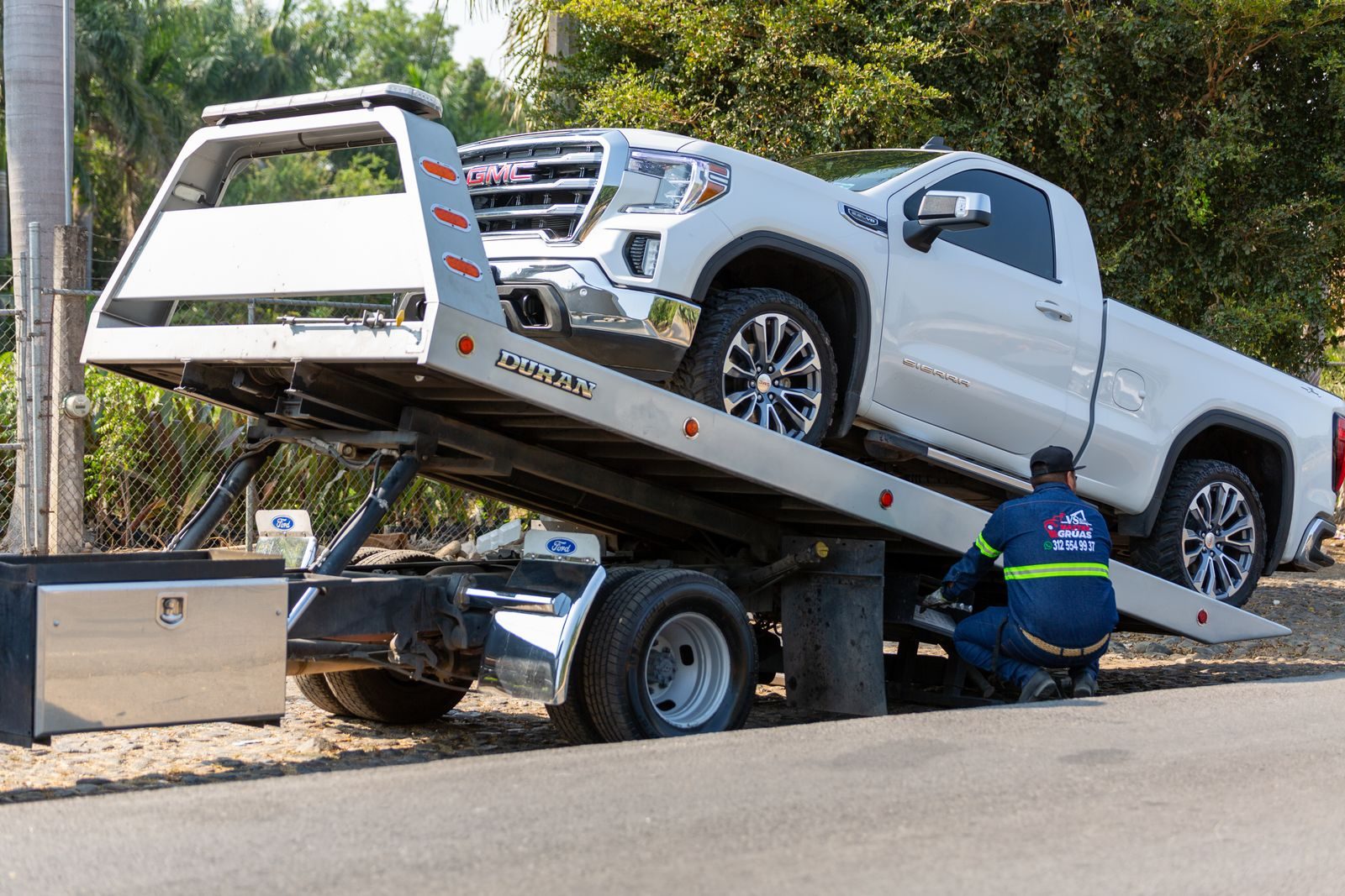Tow truck operator loading white GMC pickup truck on street in daytime