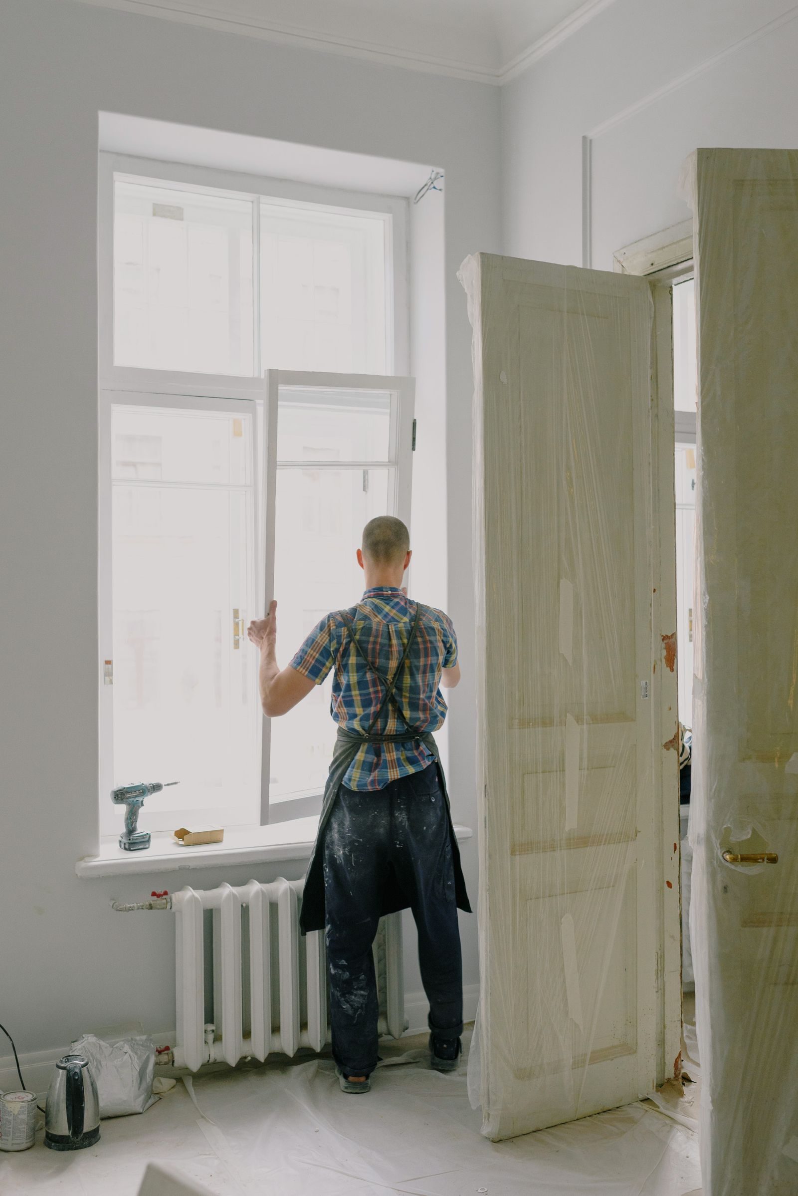 Back view of unrecognizable workman installing window near professional instruments and radiator in room durin