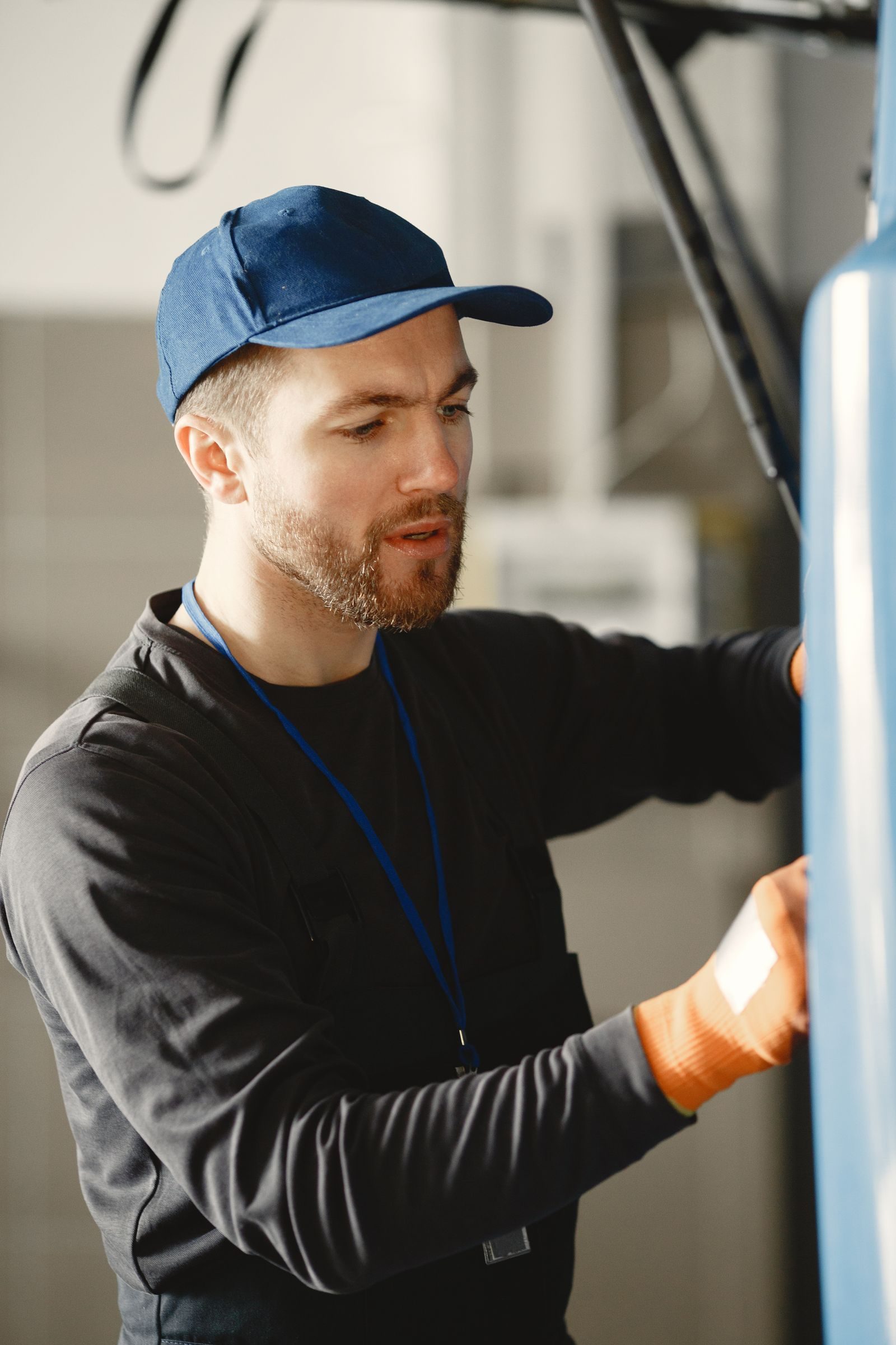 A male mechanic in a blue cap works on a vehicle indoors, focusing intently